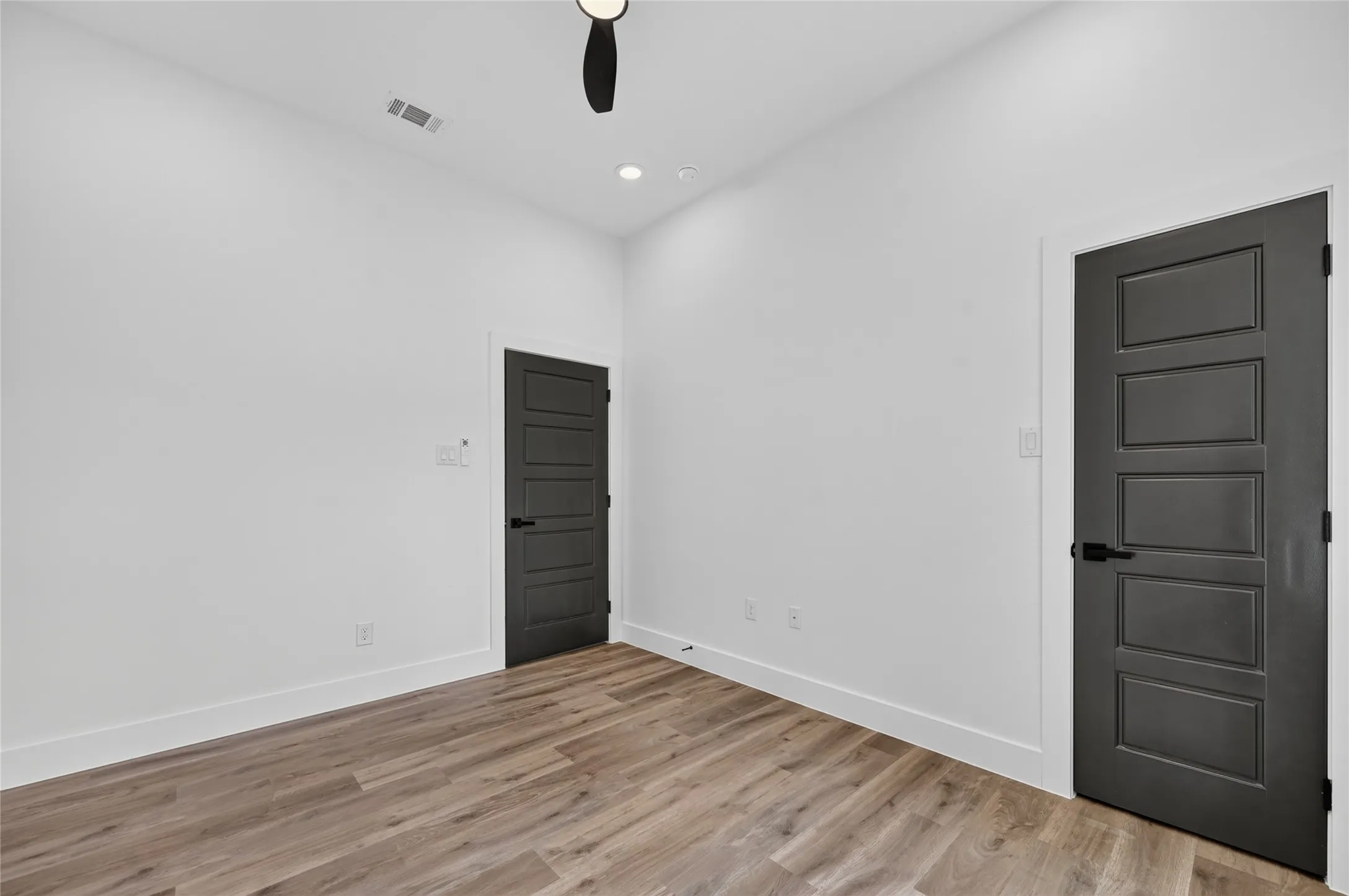 Room featuring neutral white walls, wood-finish flooring, and two paneled doors with matte black hardware