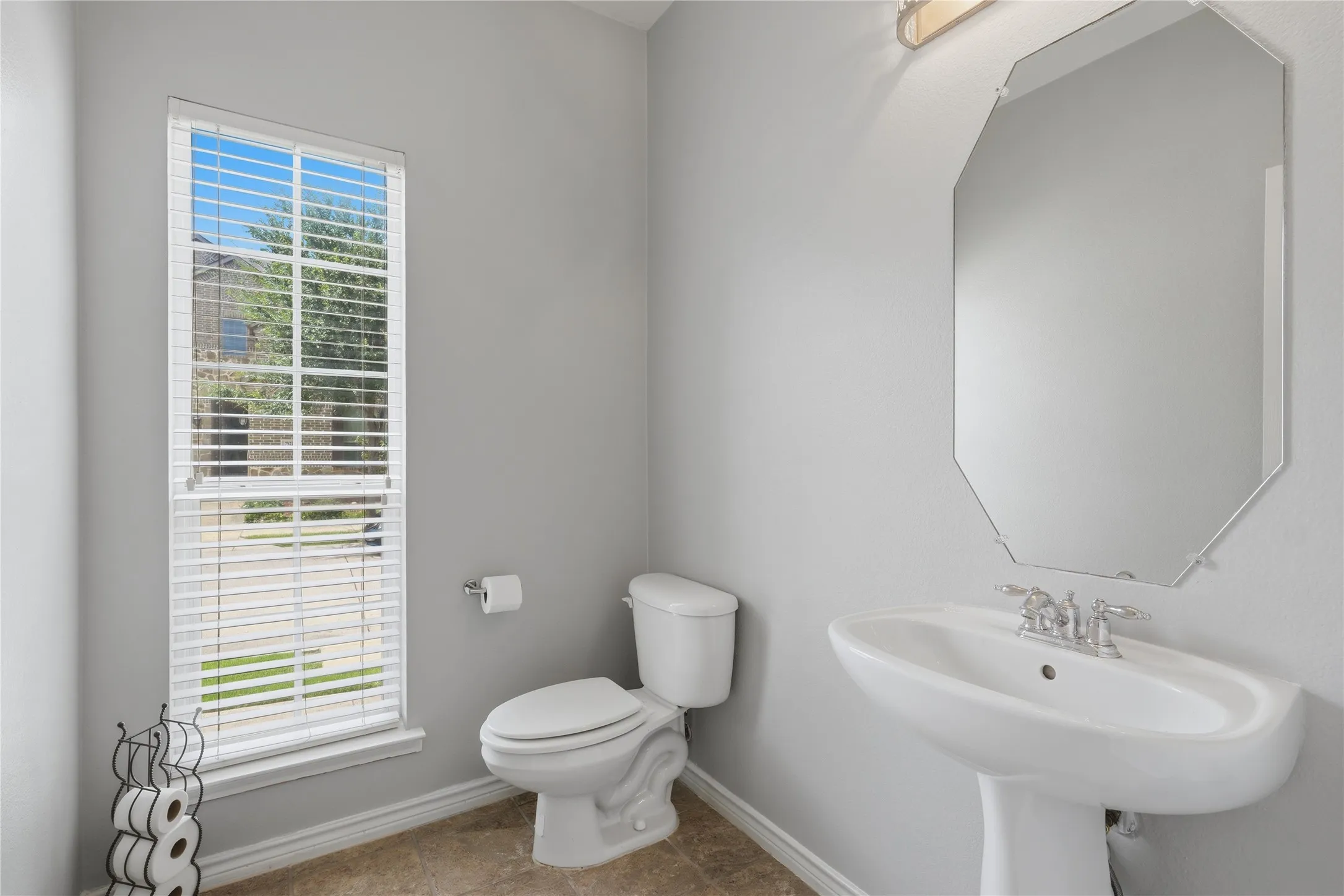 Bathroom featuring a pedestal sink, wall-mounted mirror, and window with blinds