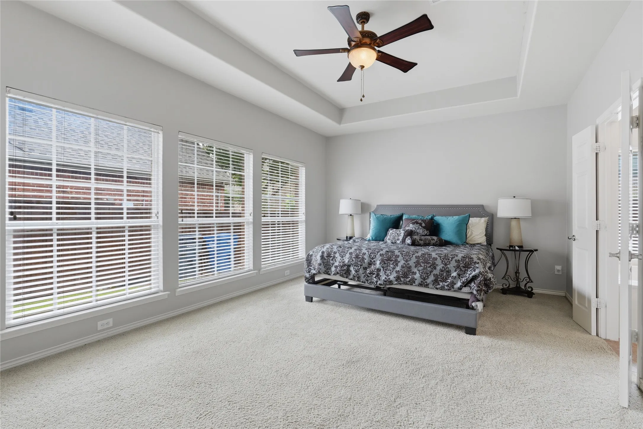 Spacious room featuring a tray ceiling, ceiling fan with integrated lighting, triple window array, and soft neutral carpeting