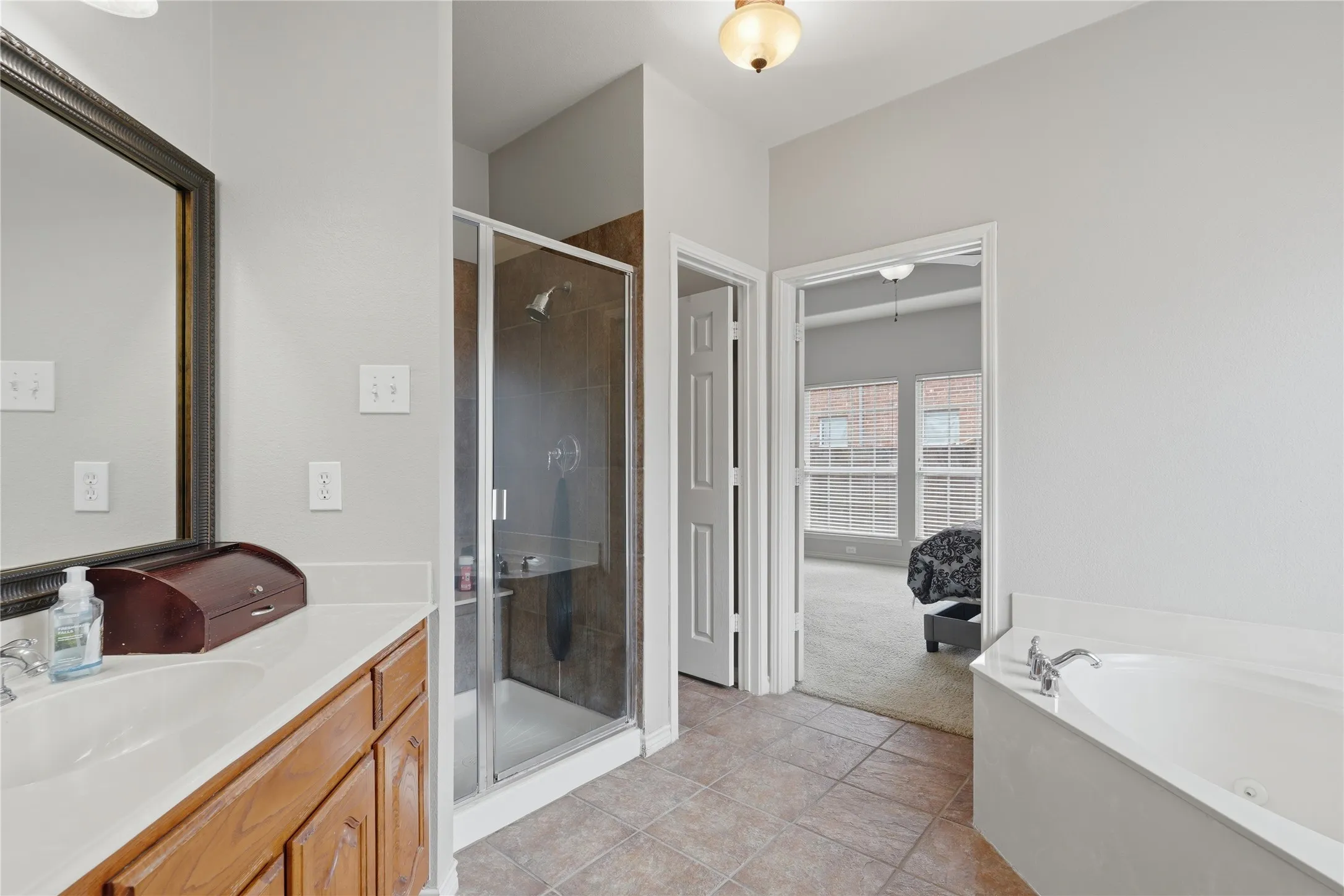 Bathroom featuring a glass-enclosed shower, a built-in tub with deck-mounted fixtures, and a vanity with a white countertop and wood cabinetry