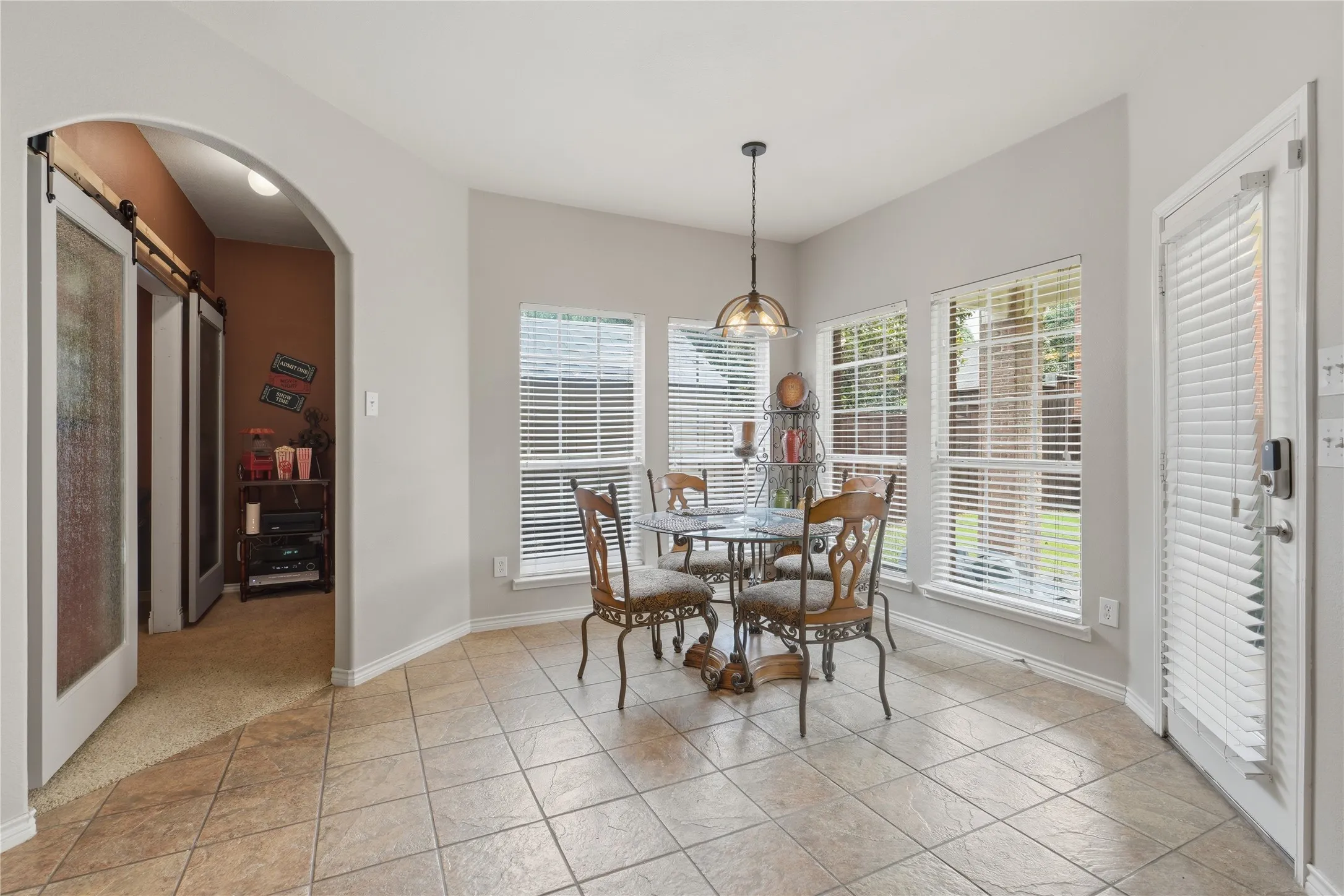 Dining area featuring large tile flooring, multiple windows with blinds, and a contemporary pendant light fixture