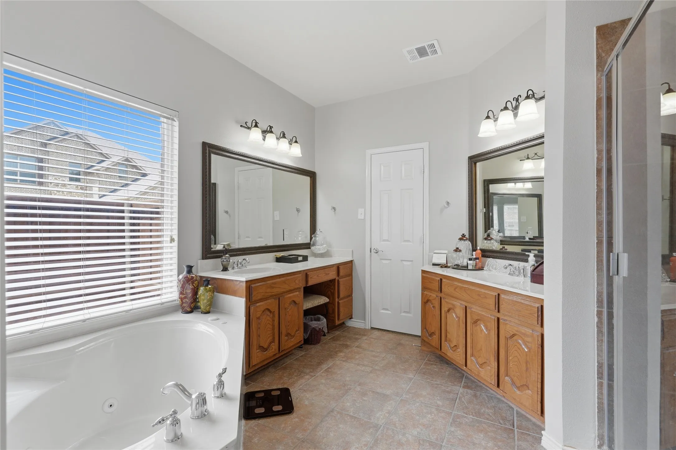 Spacious bathroom featuring a white soaking tub with chrome fixtures, a large window with horizontal blinds, and a tiled floor