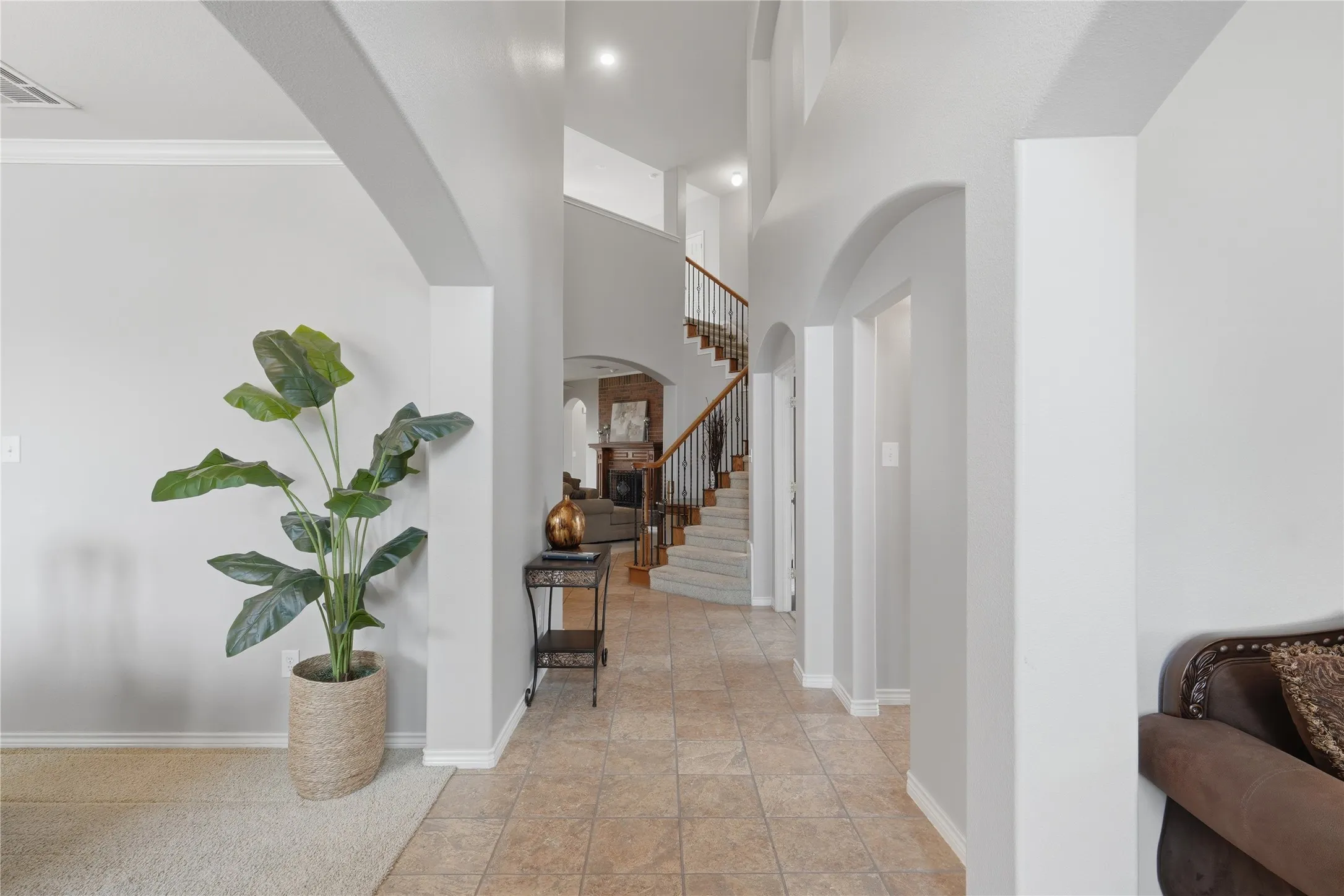 Spacious entryway featuring neutral tile flooring, high ceilings, arched doorways, a carpeted staircase with wood handrails, and a second-story landing with an open railing
