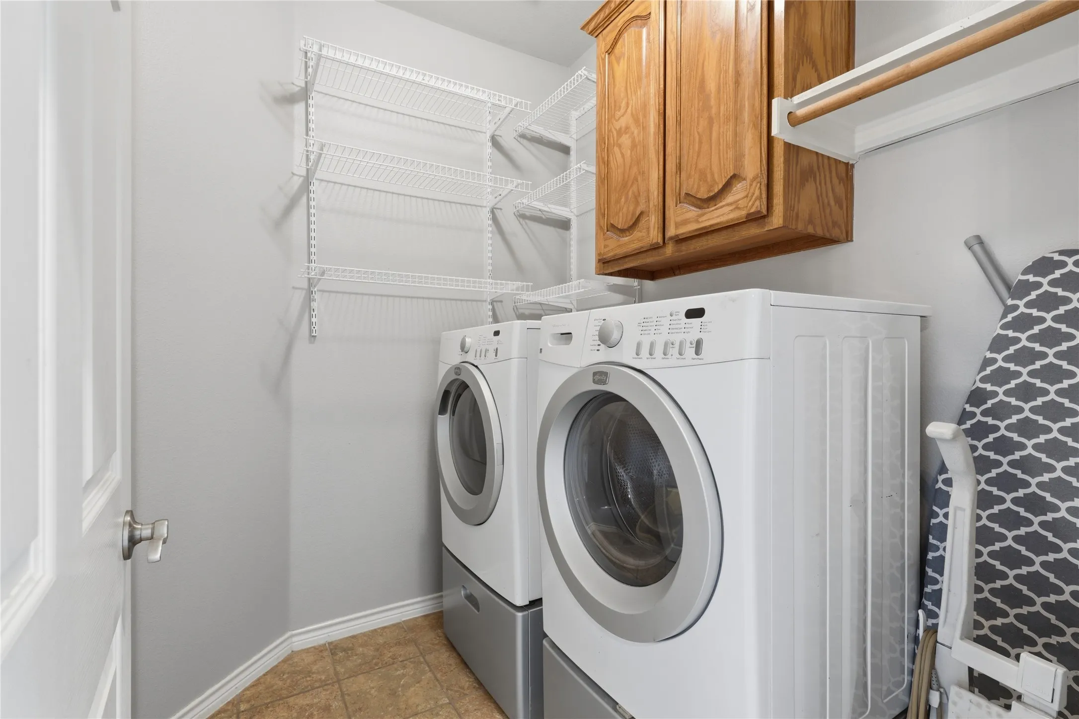 Dedicated laundry area featuring tile flooring, white wire shelving, wood cabinetry, and a clothing rod