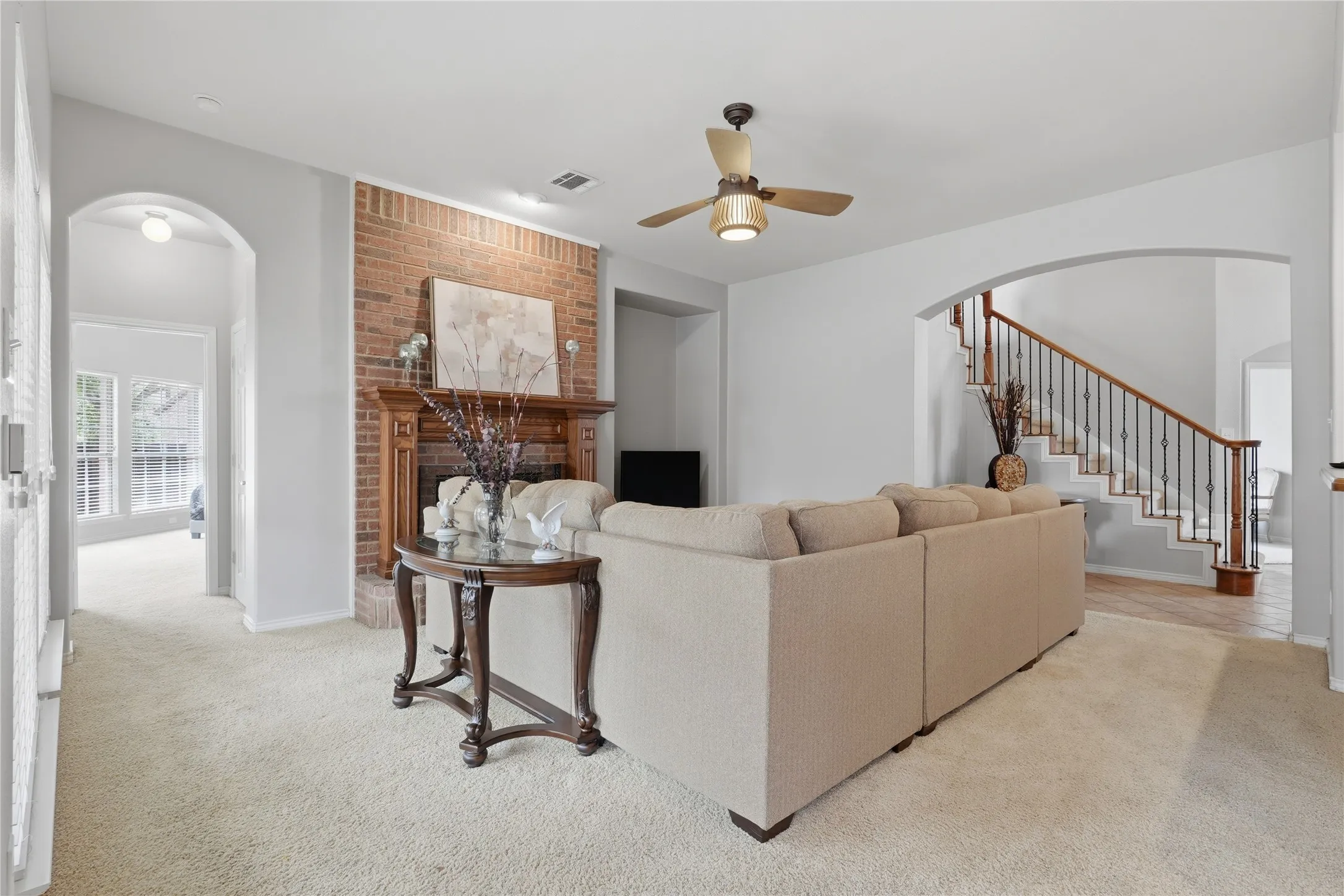Living room featuring a brick fireplace with a wood mantel, a ceiling fan, and carpet flooring