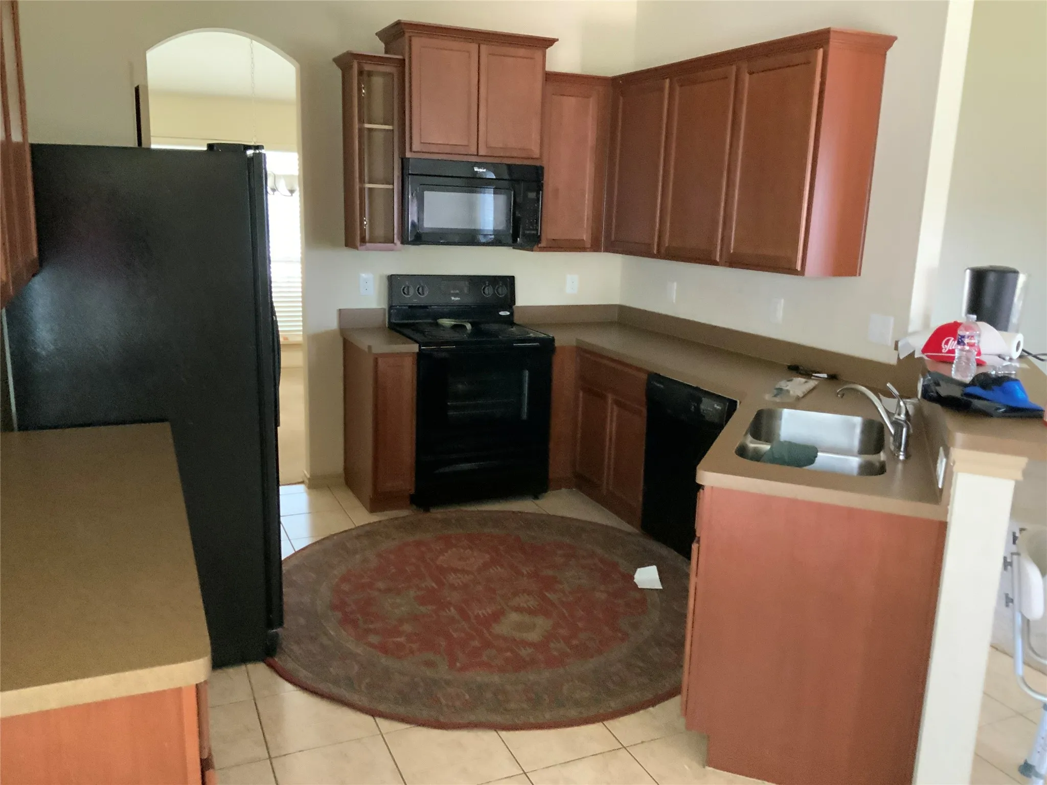 Kitchen featuring wood-finish cabinetry, black appliances, a double basin stainless steel sink, and light-toned countertops