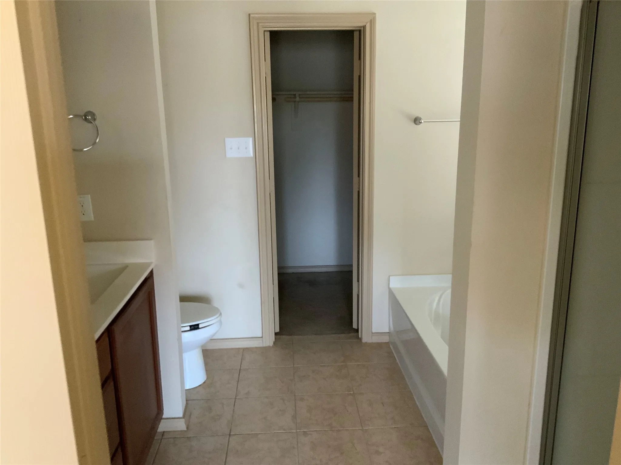 Bathroom featuring tiled flooring, a built-in tub with a white surround, a vanity with a dark wood-finish cabinet and light-toned countertop, and a white toilet