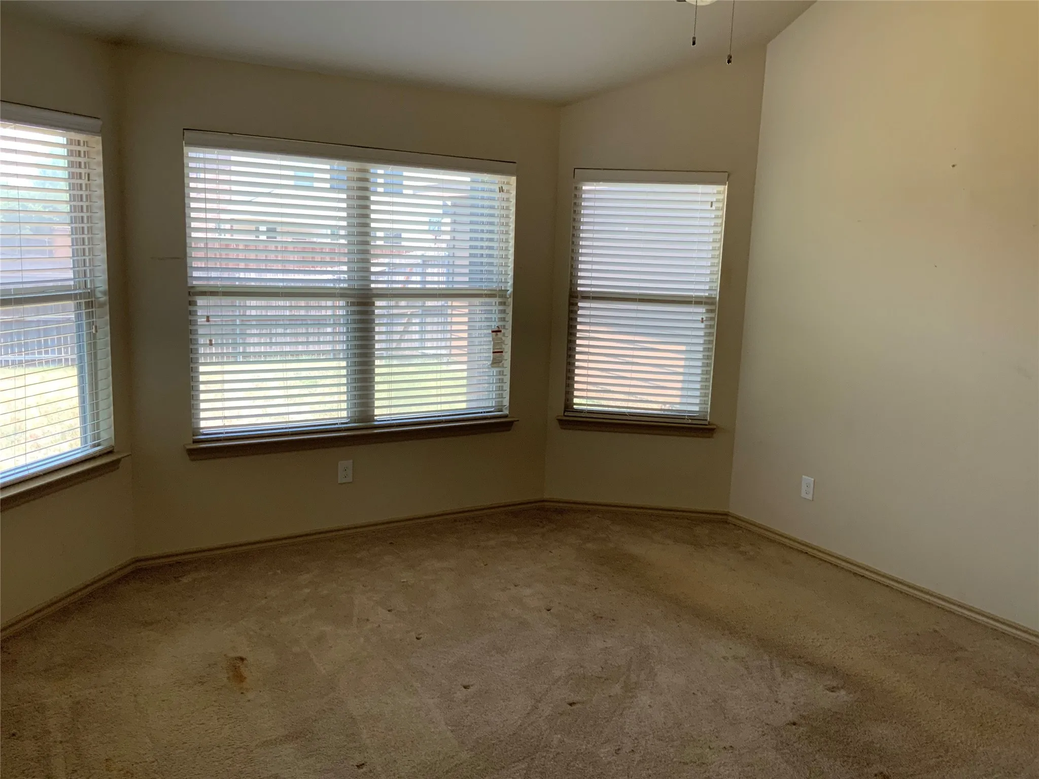 Carpeted room featuring multiple windows with blinds, a vaulted ceiling, and a ceiling fan