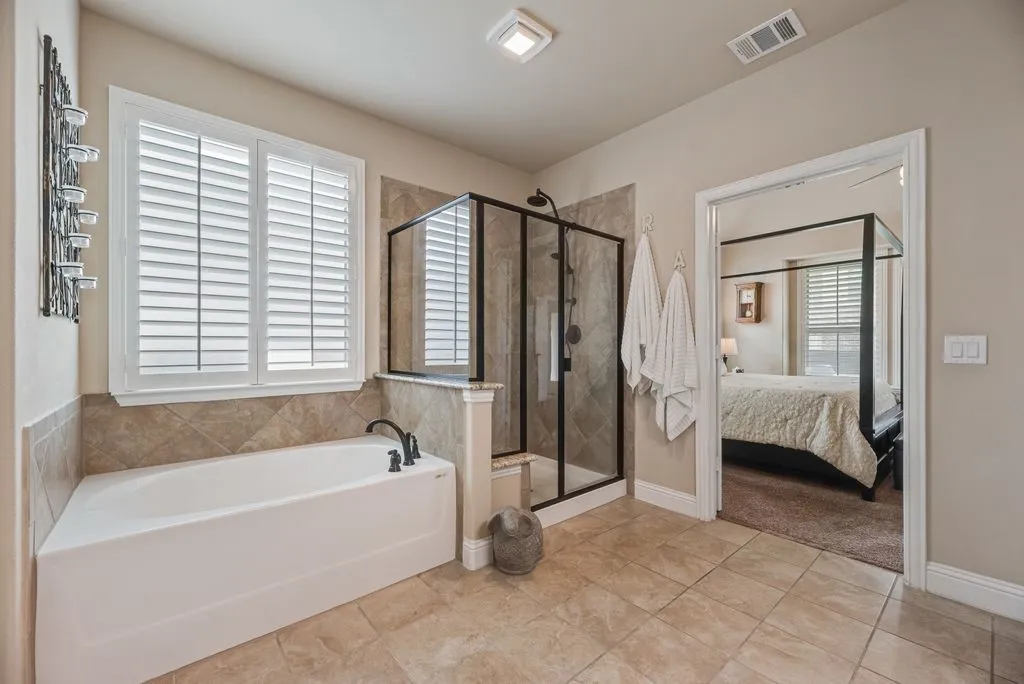 Partial View of Large Primary Bathroom. Upgraded Tile Flooring and Tub and Shower Surround. Approximately 18 inch wide built in Granite shower bench. Garden Tub, Frosted Glass and Shutter Blind Window Covering.