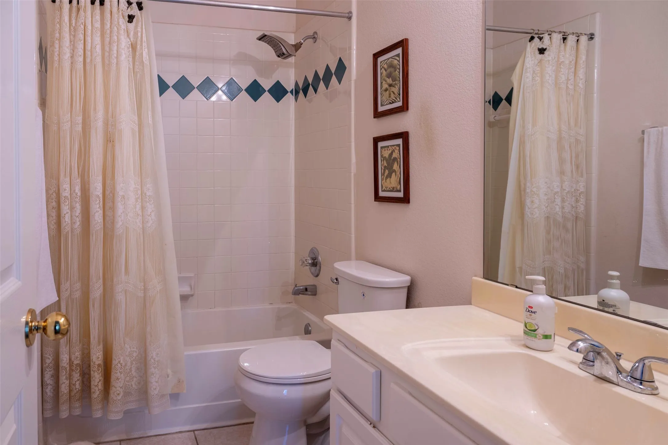 Bathroom featuring a tub/shower combination with diamond-patterned accent tiles, a single vanity with a laminate countertop, and a built-in wall mirror