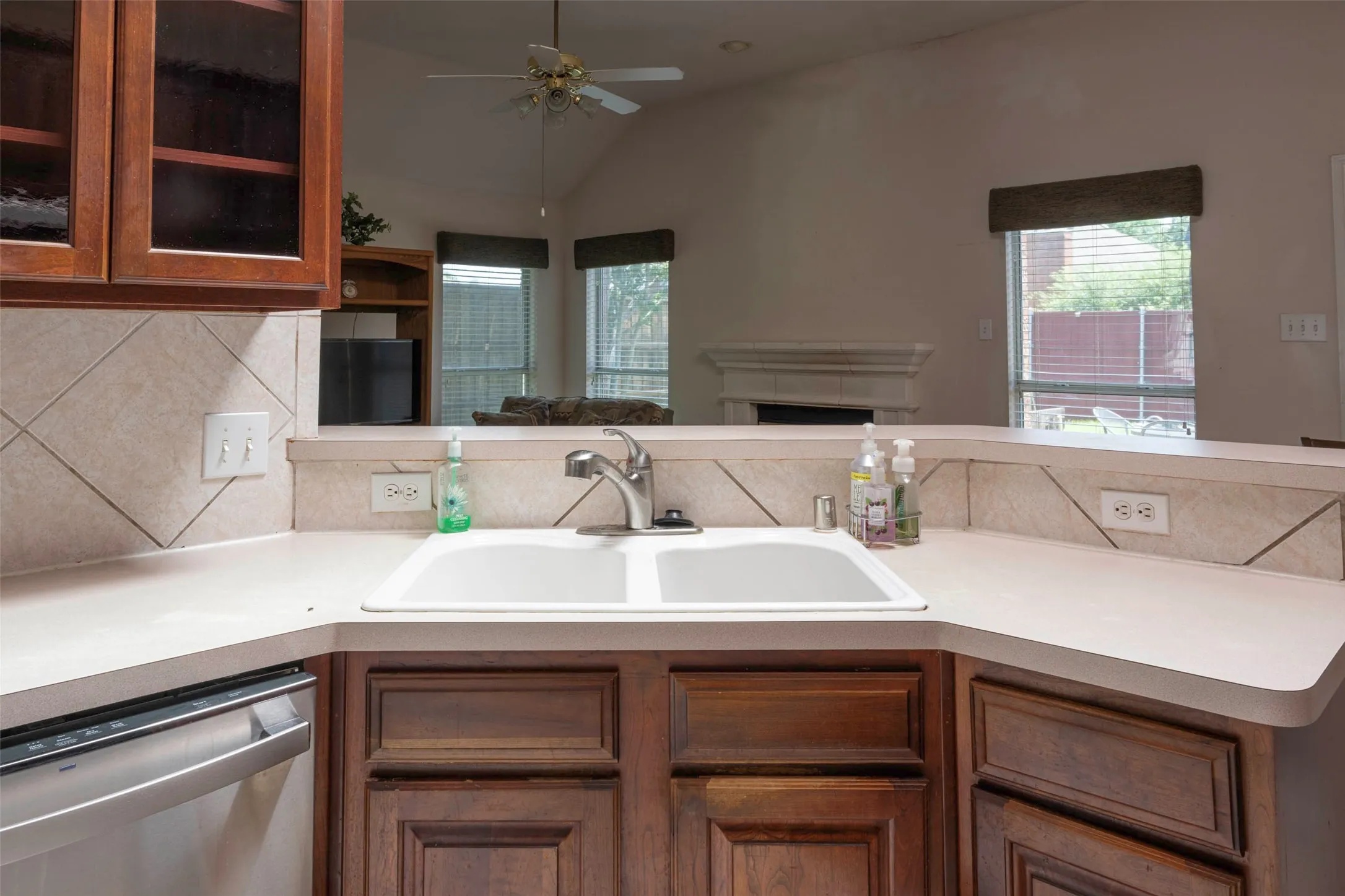 Kitchen featuring a double-basin sink, light-toned countertops, and rich wood cabinetry with glass-front uppers