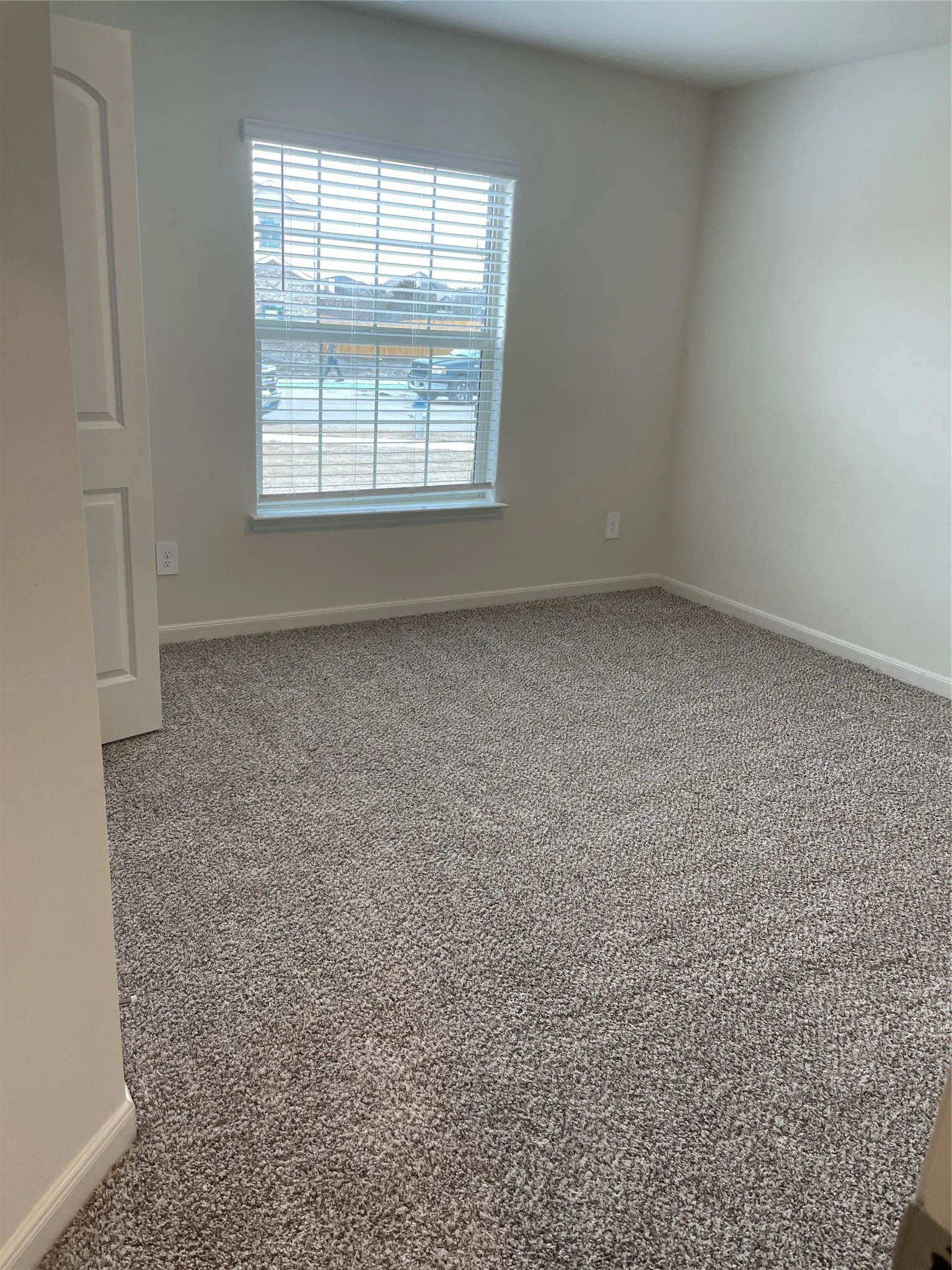 Carpeted room featuring a window with horizontal blinds, light-colored walls, white trim, and a white interior door