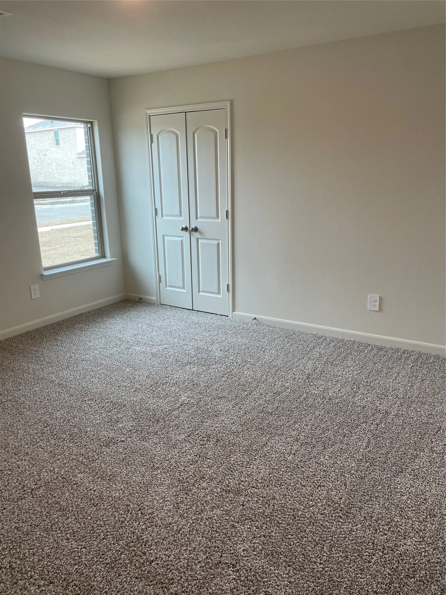 Carpeted room featuring light-toned walls, a double-door closet with paneling, and a window with white trim