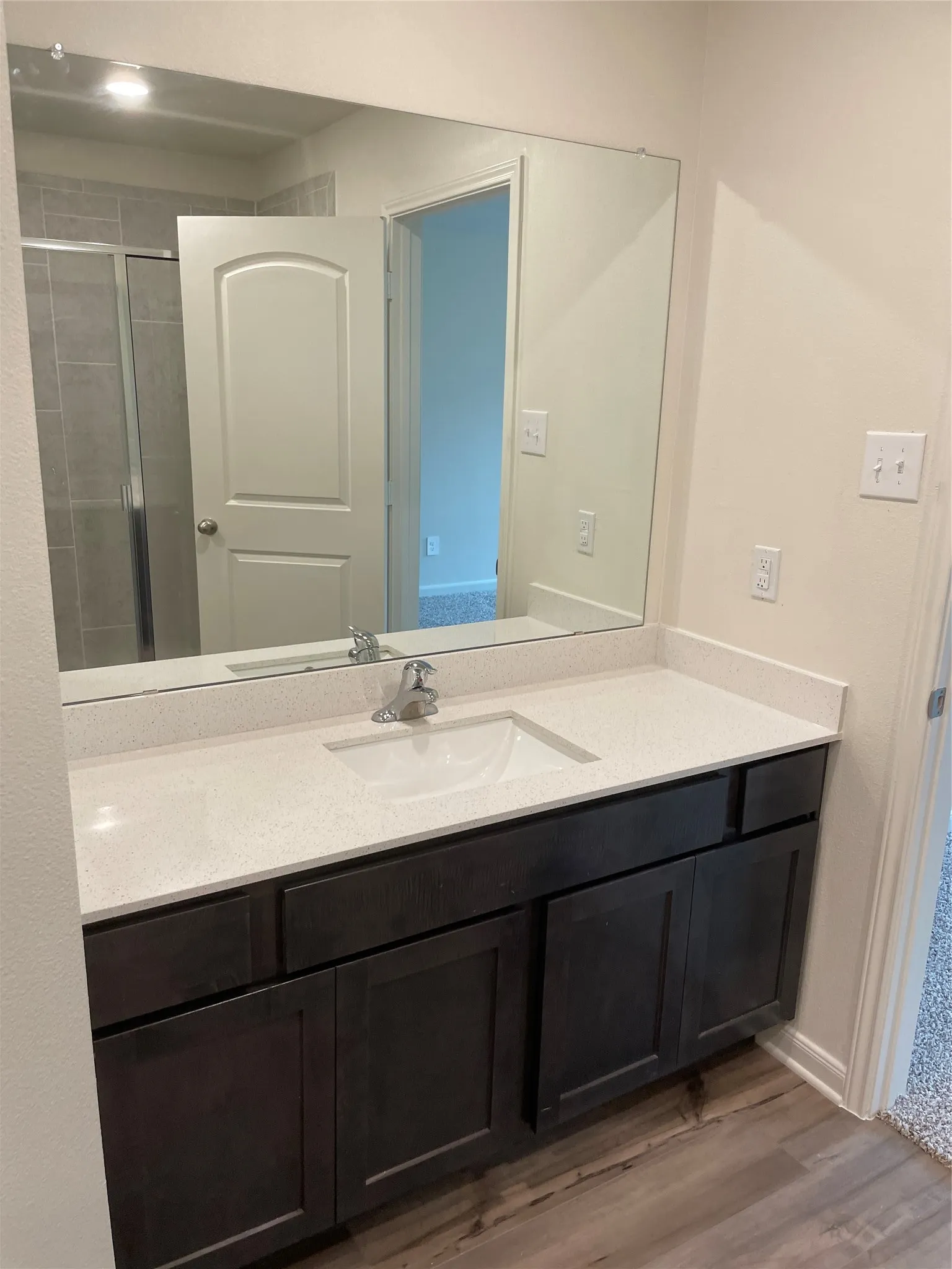 Bathroom vanity featuring a light-toned countertop with an integrated sink, dark wood-finish cabinetry, and a chrome faucet