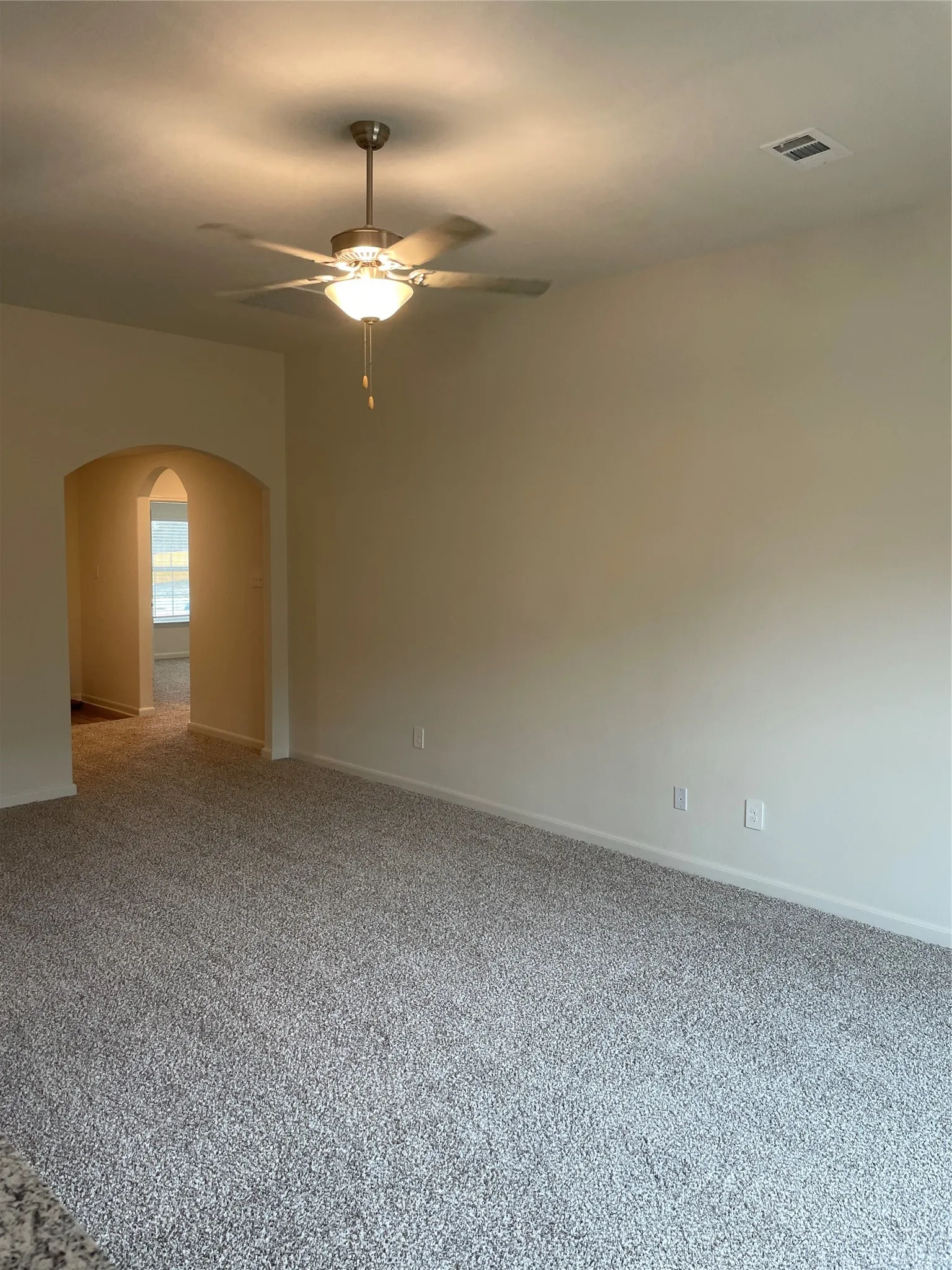 Spacious room featuring neutral carpeting, light-toned wall paint, and a ceiling fan with integrated lighting