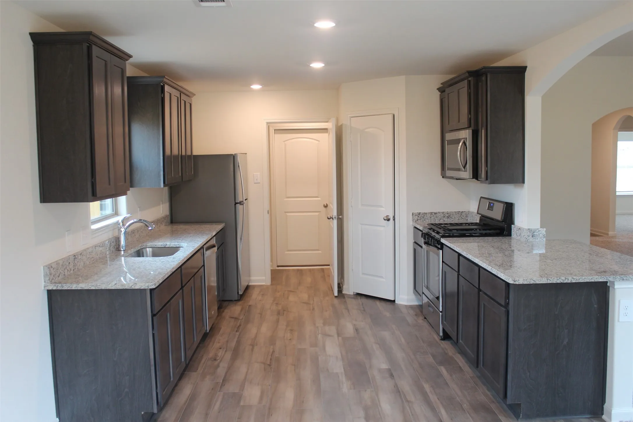 Contemporary kitchen featuring dark wood-finish cabinetry, light speckled countertops, stainless steel appliances including a gas range and built-in microwave, and wood-finish flooring