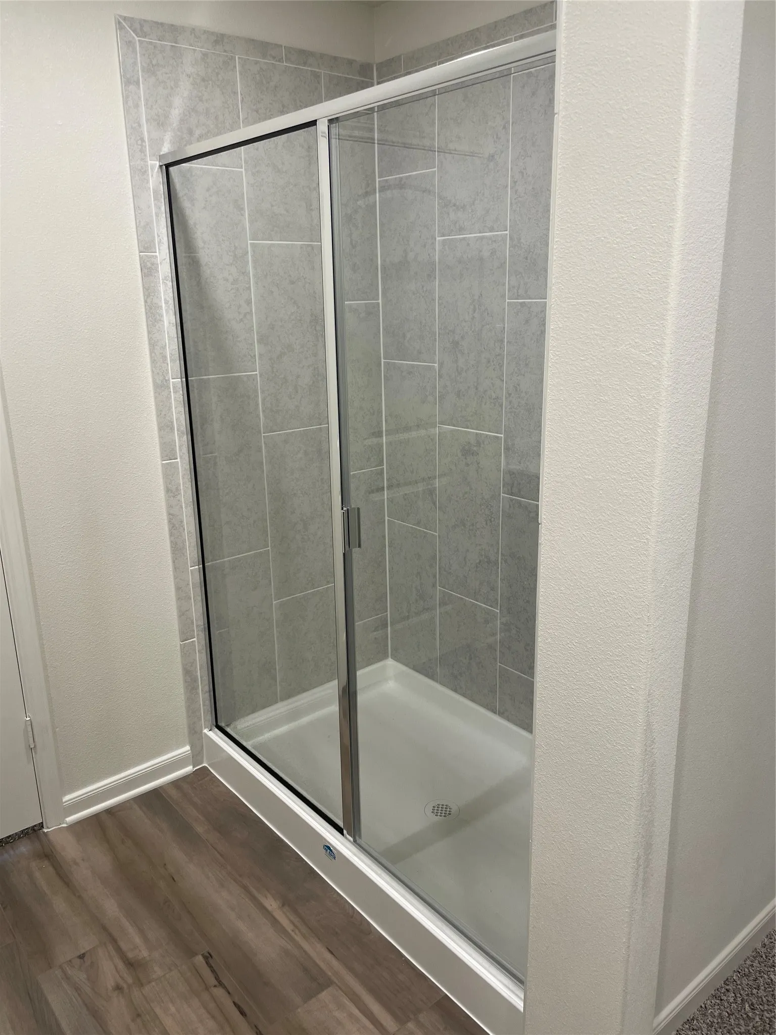 Glass-enclosed shower with a white base, vertical gray tile surround, and chrome-finish hardware