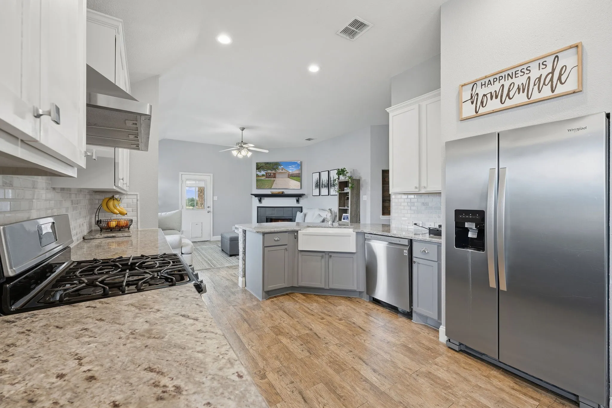 Open-concept kitchen featuring wood-finish flooring, stainless steel appliances, white upper cabinetry, and a white subway tile backsplash