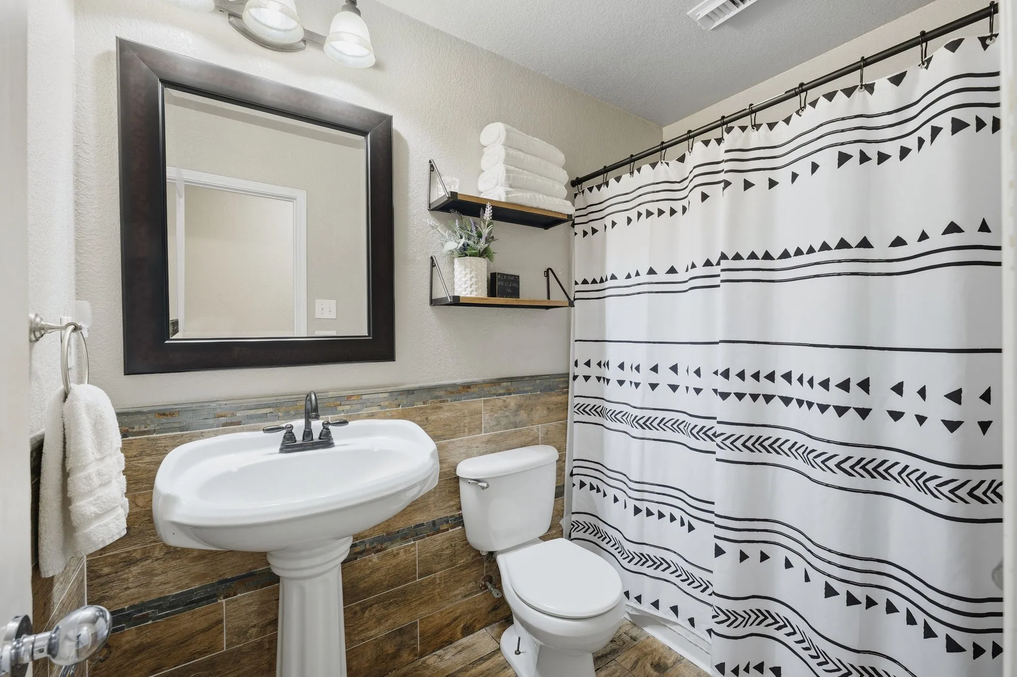 Pedestal sink with dark-toned faucet, framed mirror, and warm-toned tile wainscoting