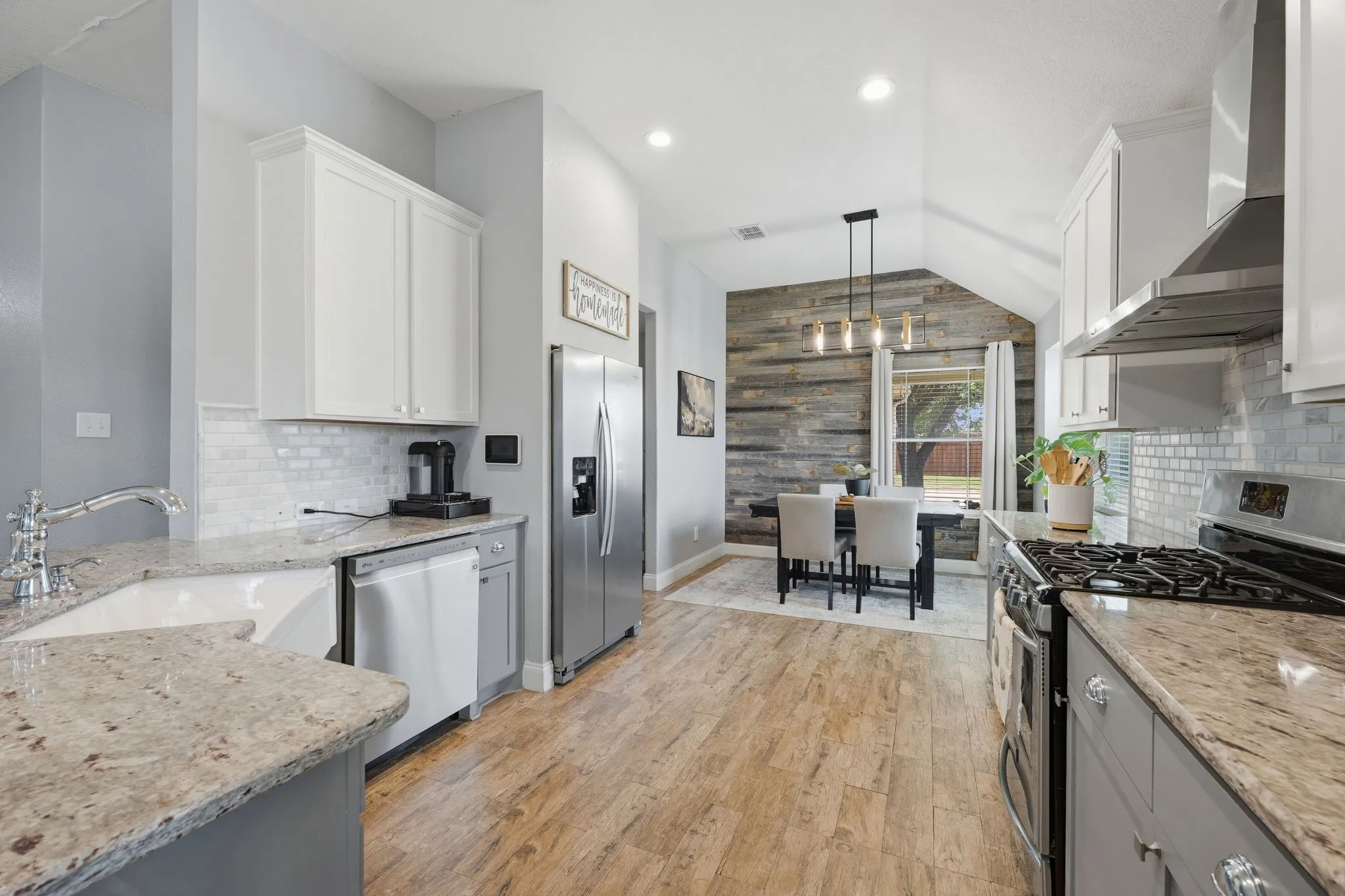 Kitchen featuring wood-finish flooring, white cabinetry, granite countertops, a farmhouse sink, and stainless steel appliances including a refrigerator and gas range