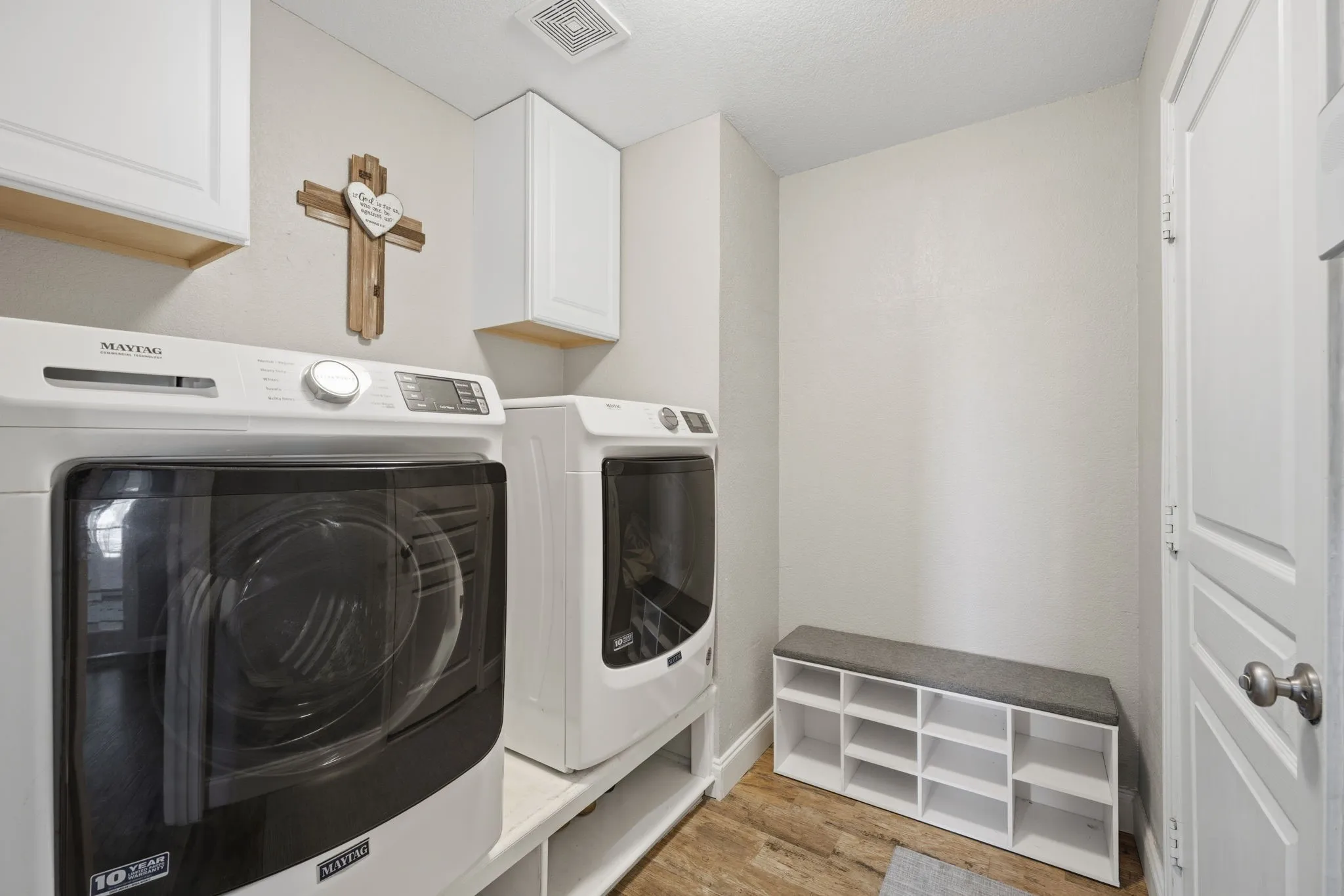 Dedicated laundry area featuring wood-finish flooring, white cabinetry, and a storage bench with shelving