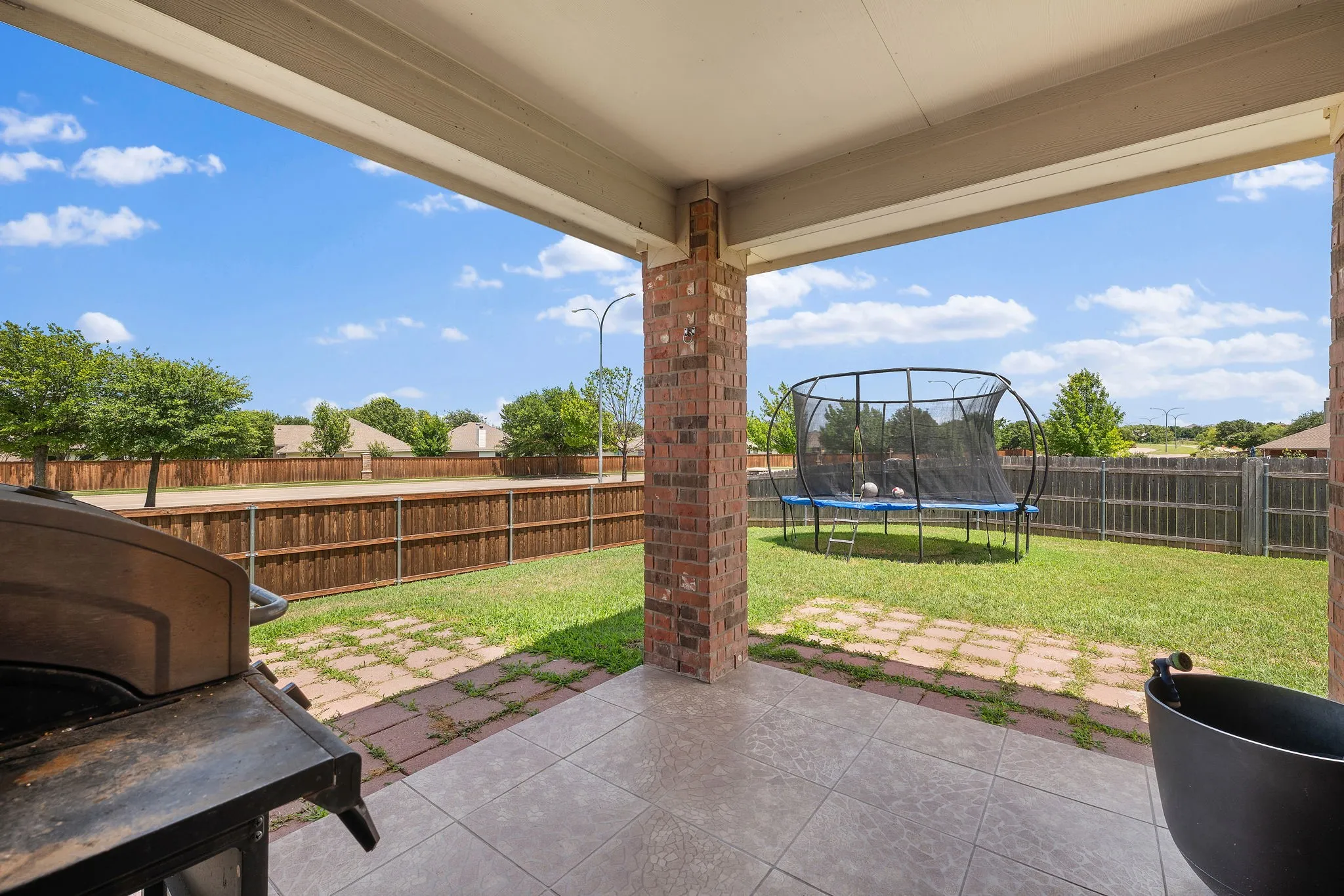Covered patio with tile flooring, brick columns, and a wooden privacy fence enclosing a grassy yard