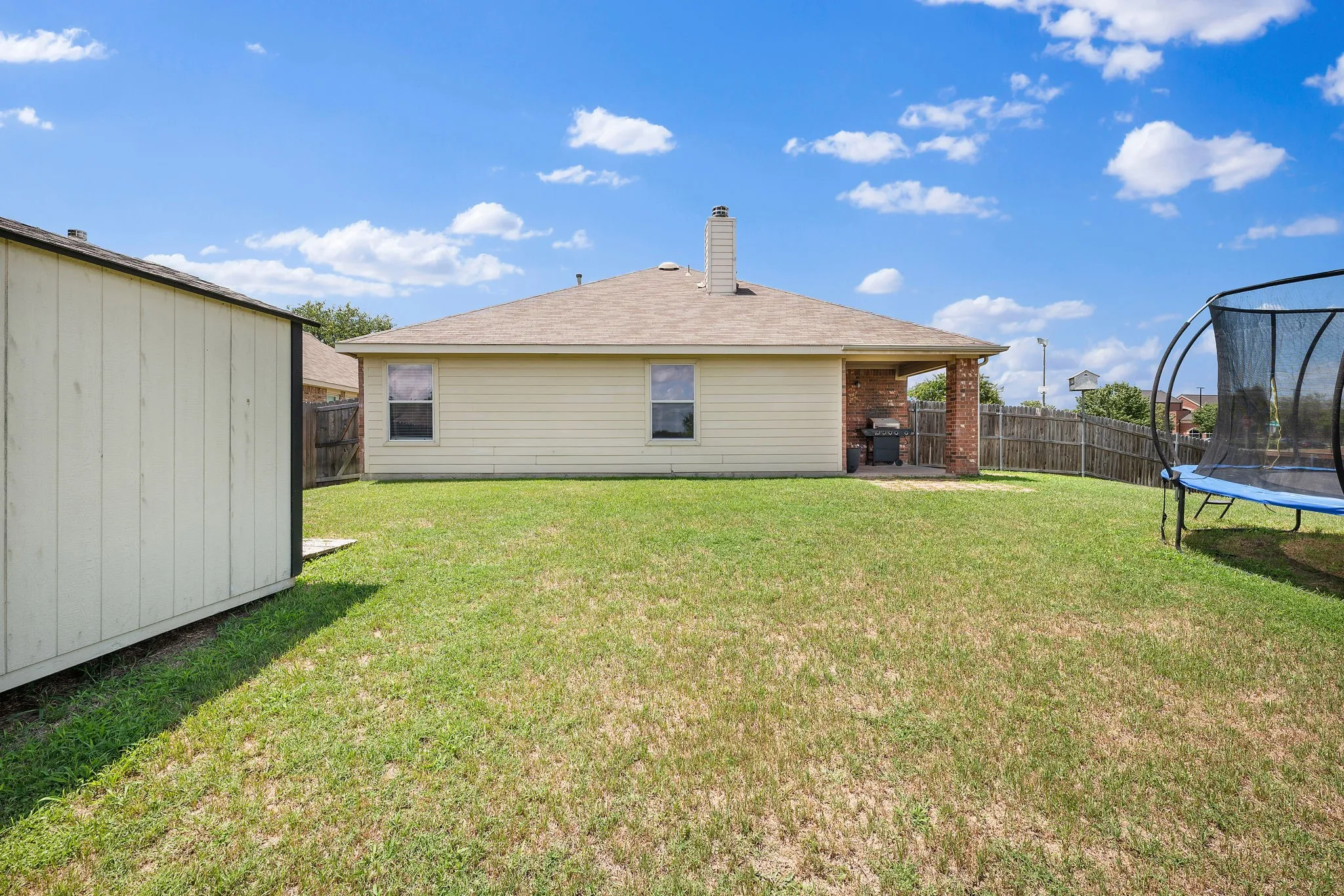 Spacious backyard with a covered patio featuring brick columns, a wood fence perimeter, and a detached storage shed