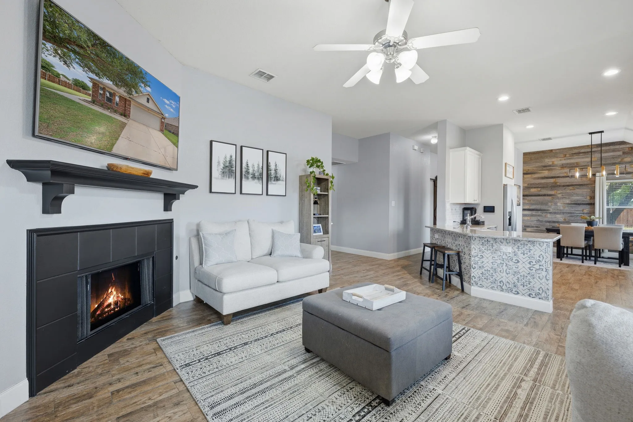 Living area featuring wood-finish flooring, a corner fireplace with a black tile surround and mantle, and a ceiling fan