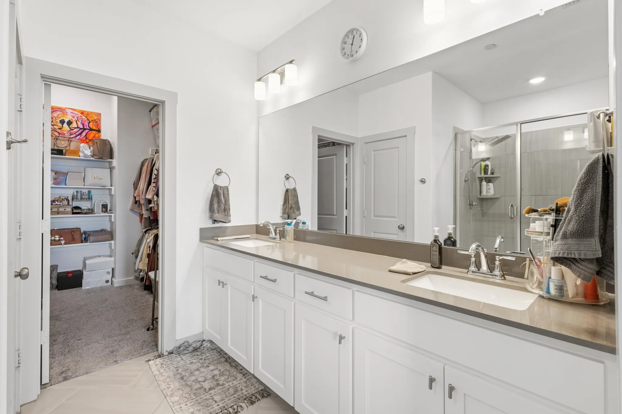Spa-inspired primary bathroom featuring a dual vanity with white cabinetry, quartz stone countertops, dual sinks, and designer chrome fixtures for a luxurious daily routine.