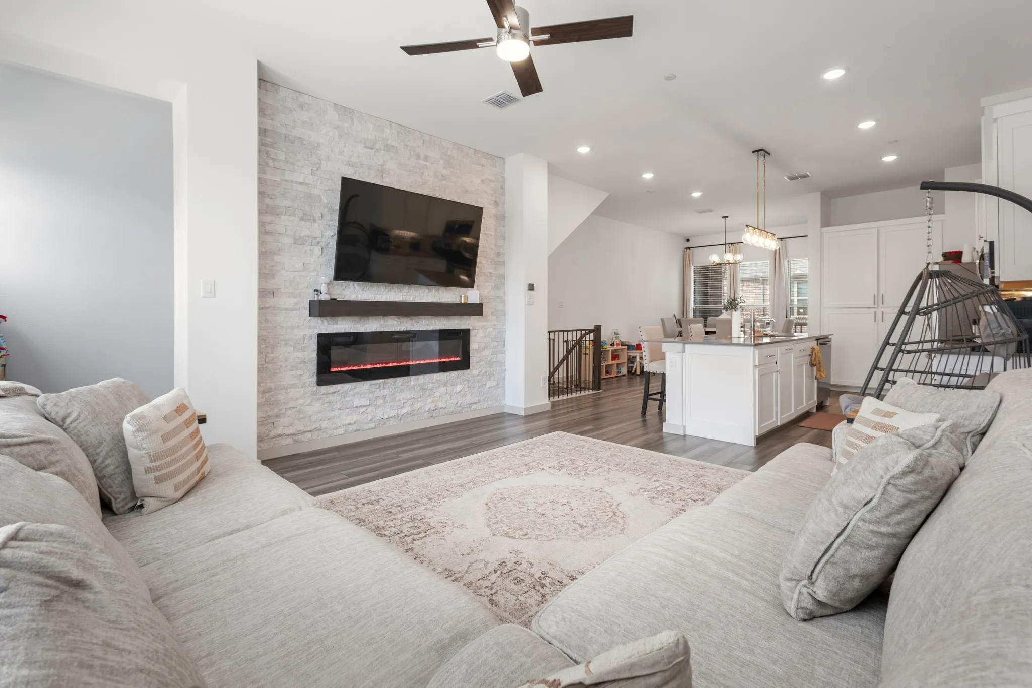 Spacious main living area featuring a large-format linear fireplace set into a striking stone accent wall, luxury vinyl plank flooring, and abundant natural light through oversized windows.