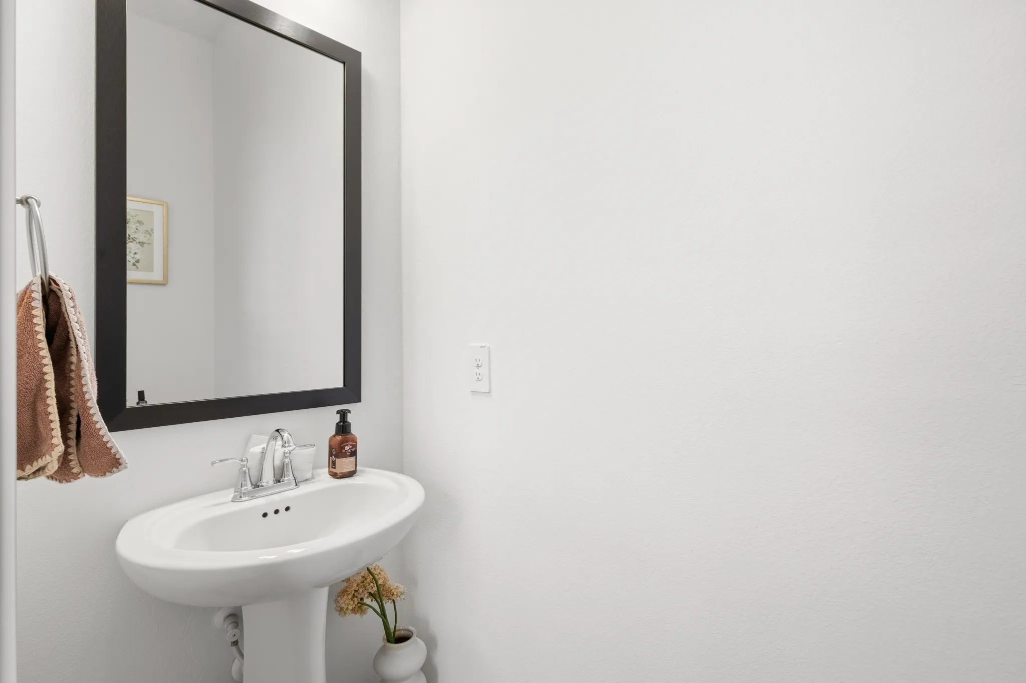 Elegant powder room featuring a pedestal sink with chrome faucet, a large framed mirror, and minimalist design -- conveniently located on the main living level for guests.