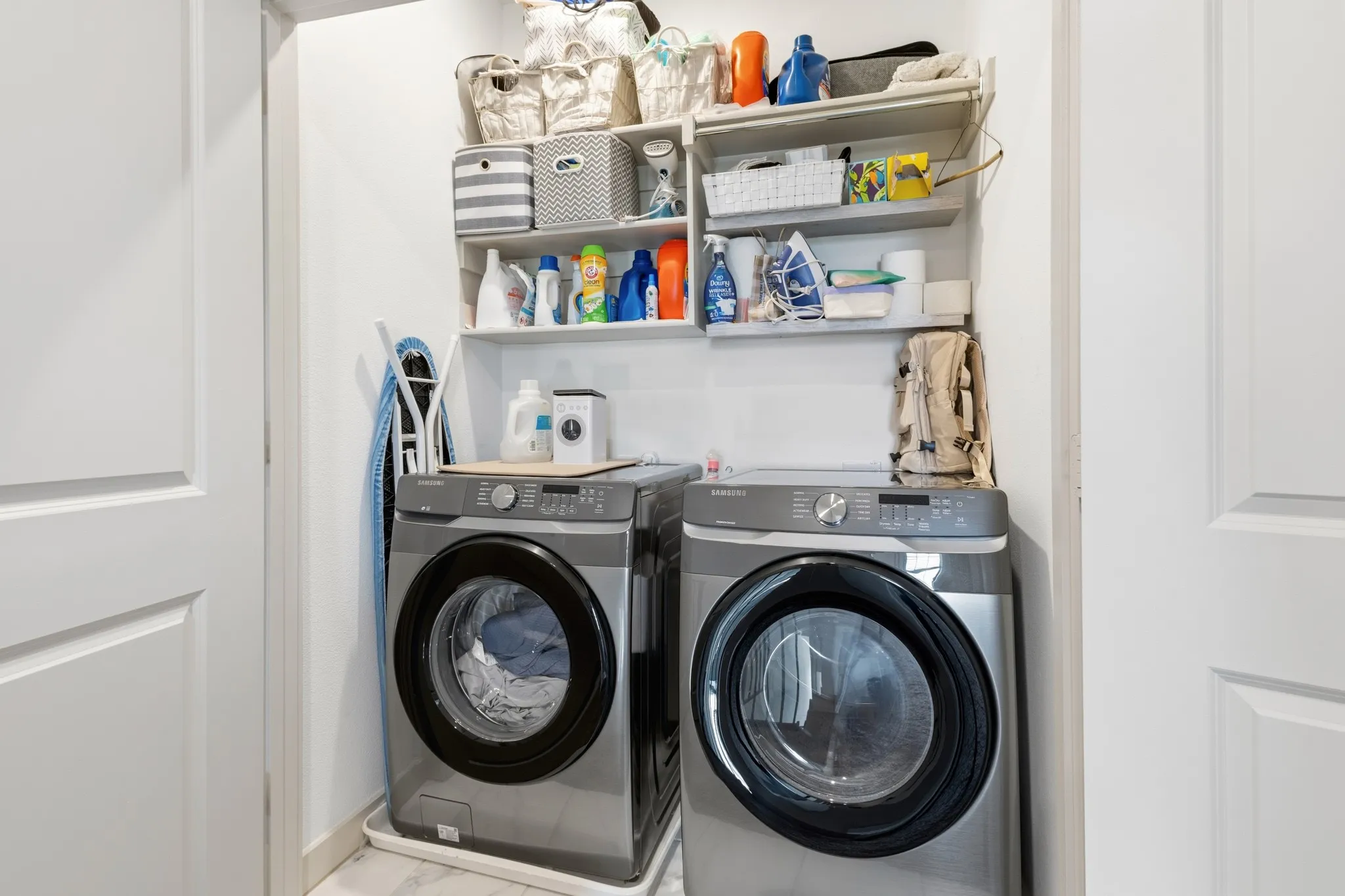 Dedicated laundry closet with a full-size front-loading washer and dryer, built-in shelving for organization, and a clean, efficient layout making household chores effortless.