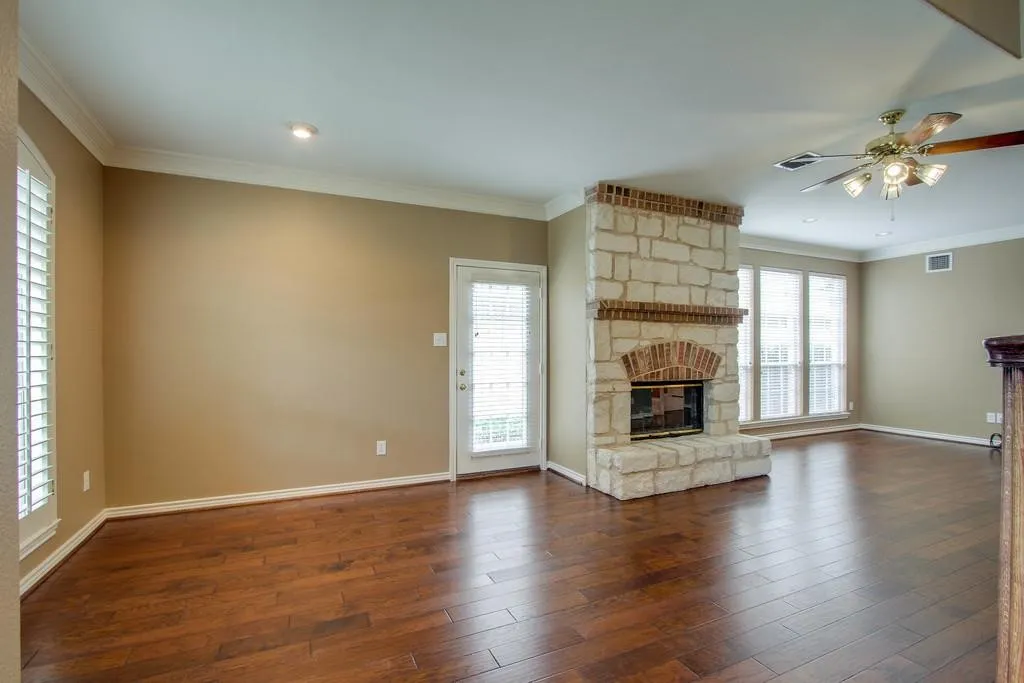 Living space featuring a stone fireplace with brick accents, wood-finish flooring, and crown molding