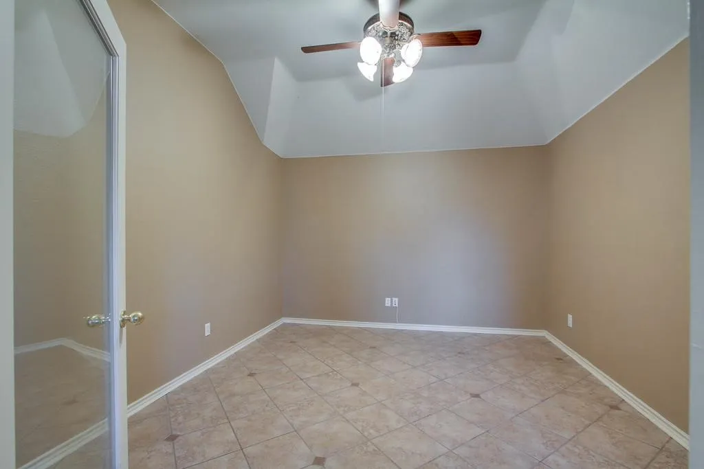 Upstairs office with glass door. Neutral tone walls with white trim, vaulted ceiling, and a ceiling fan with light fixture