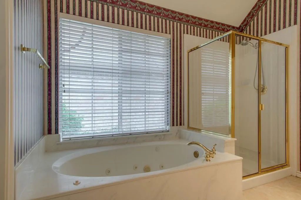 Jetted soaking tub with a surrounding marbled-finish surface, brass-finish faucet, and an adjacent glass-enclosed shower with brass-finish framing and fixtures