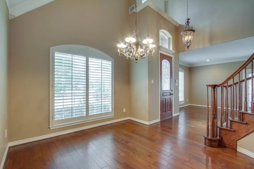 Foyer and living area featuring high vaulted ceilings, wood-finish flooring, an arched window with plantation shutters, a decorative chandelier, and a wood-paneled entry door with leaded glass