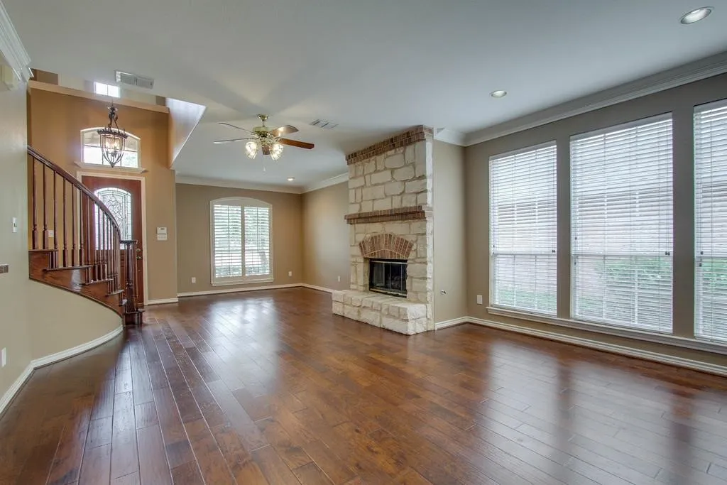 Spacious living area featuring wood-finish flooring, a stone fireplace with brick accents, and a curved wooden staircase