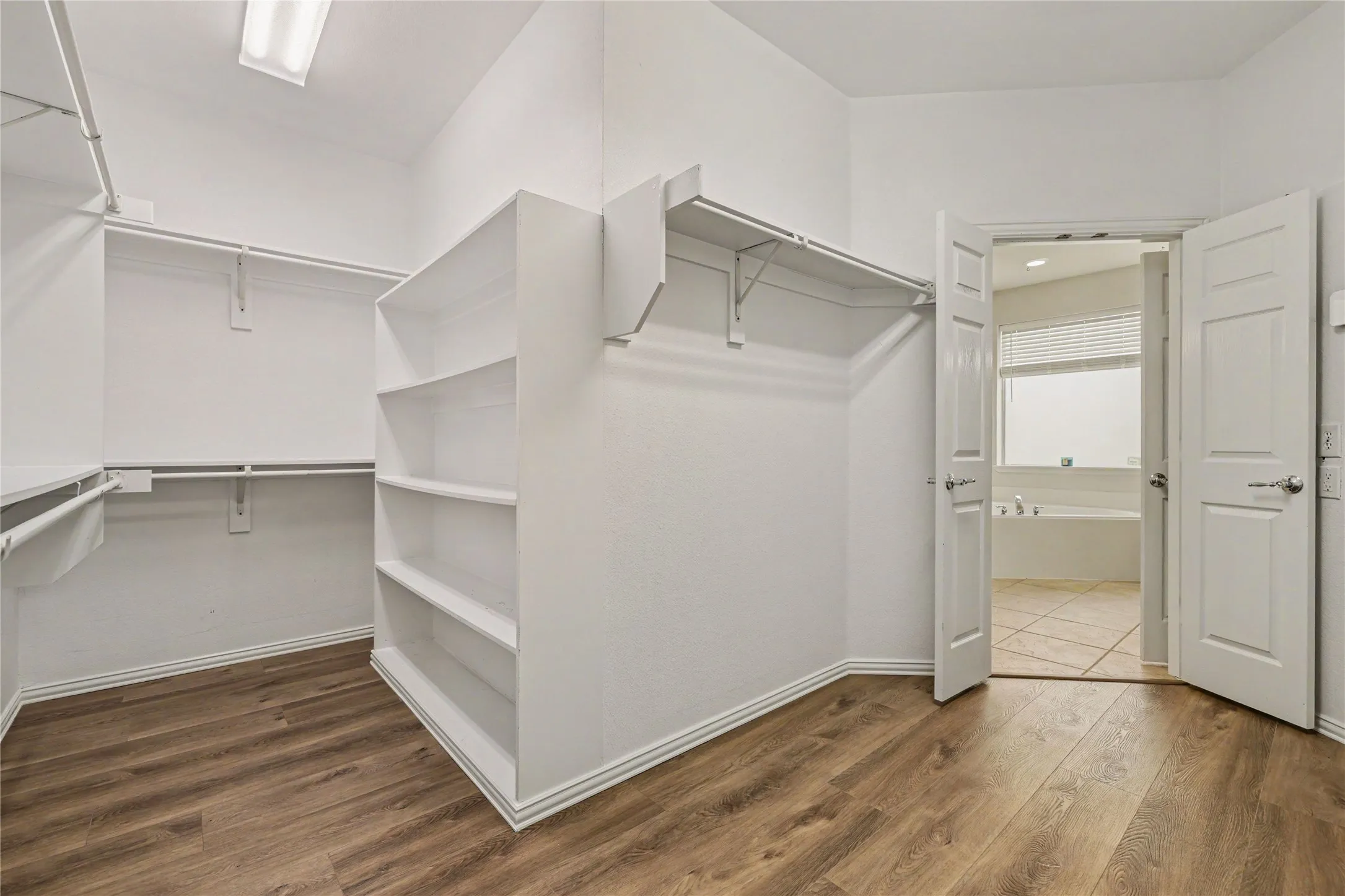 Walk-in closet with wood-finish flooring, built-in shelving, and hanging rods