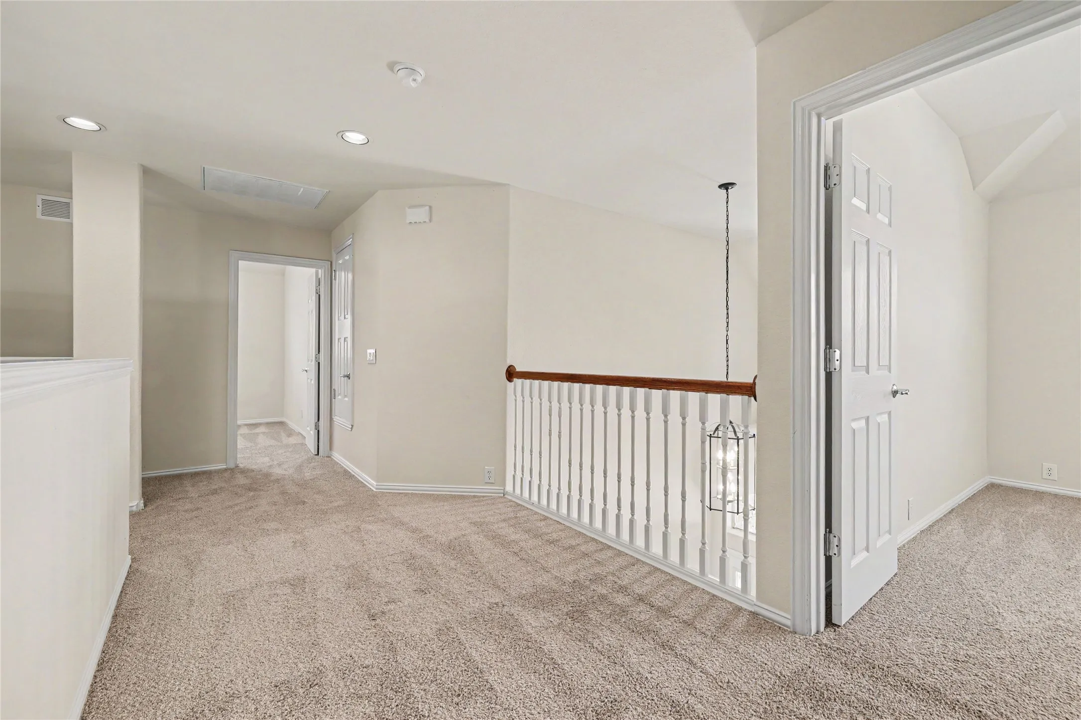 Carpeted landing area featuring a white baluster railing with a wood-finish top rail, recessed lighting, and a hanging pendant light fixture