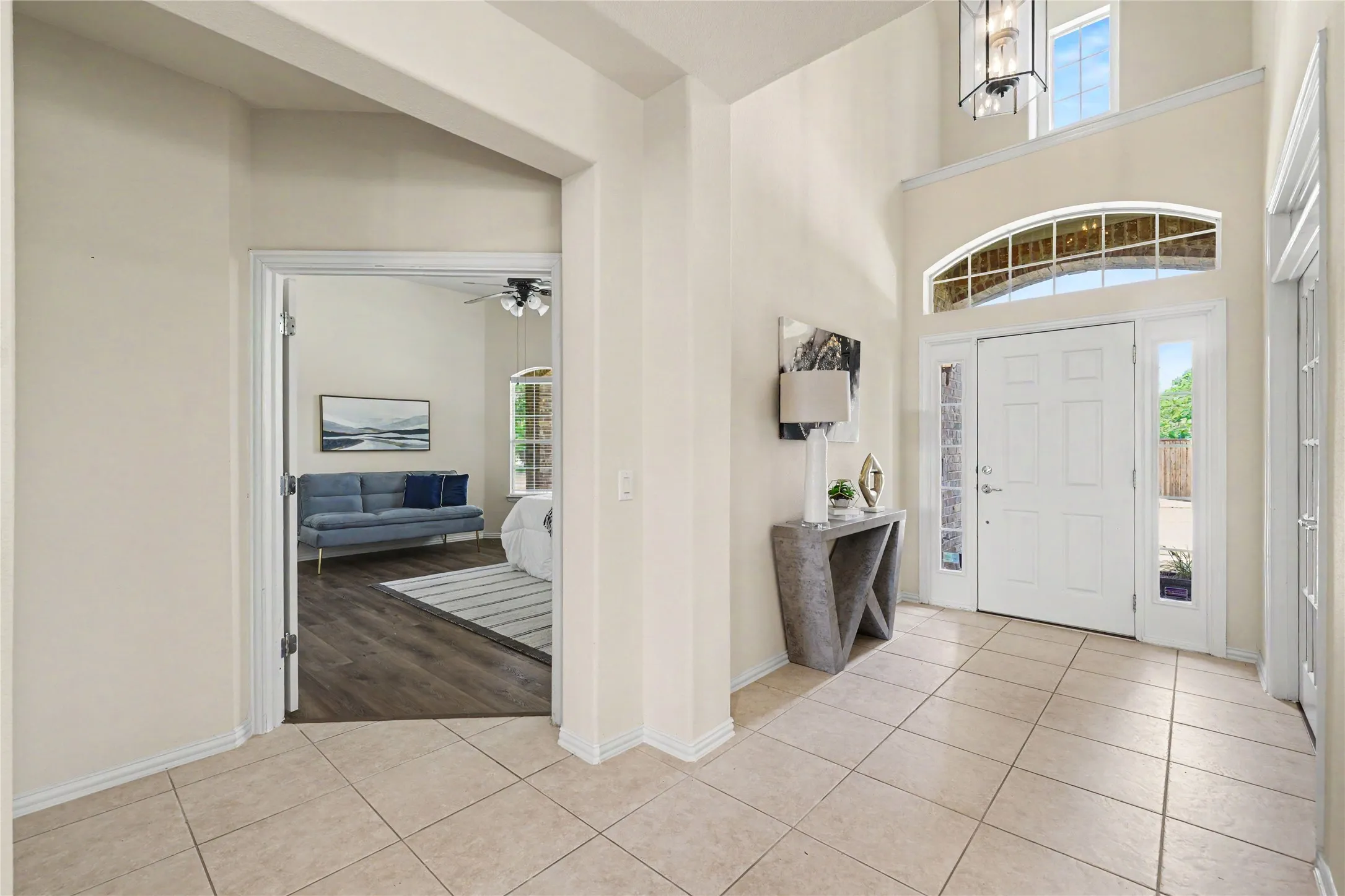 Two-story foyer featuring large format tile flooring, a paneled entry door with sidelights, and an arched transom window