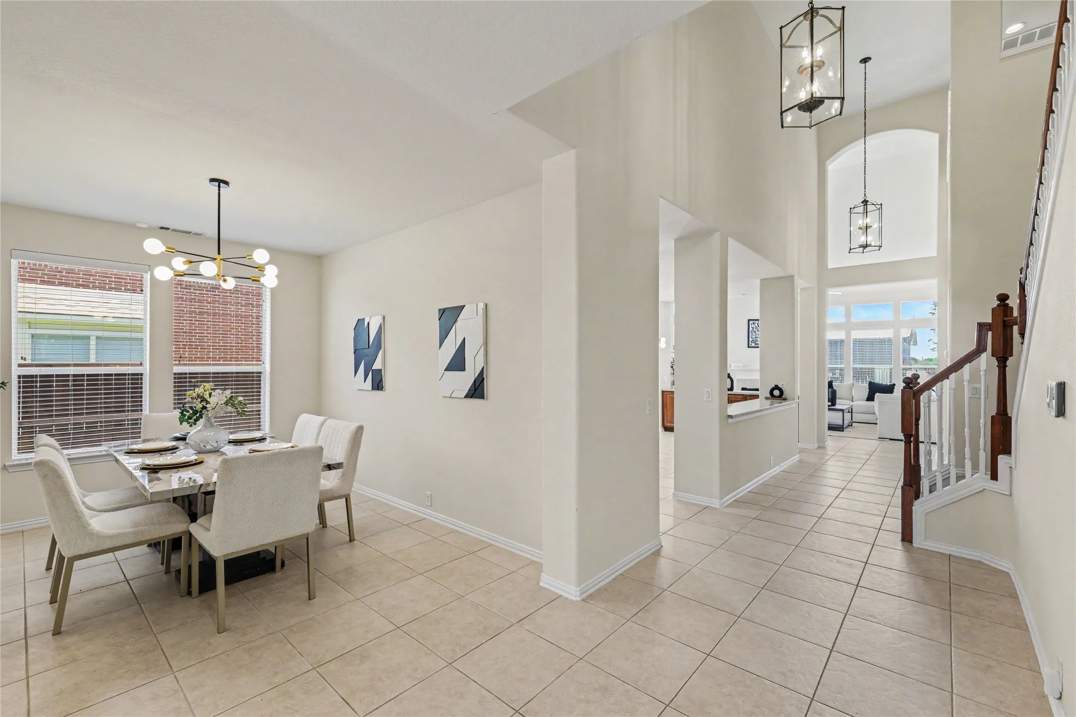 Spacious entryway featuring light tile flooring, a staircase with wood banister and white spindles, and double-height ceilings with pendant lighting