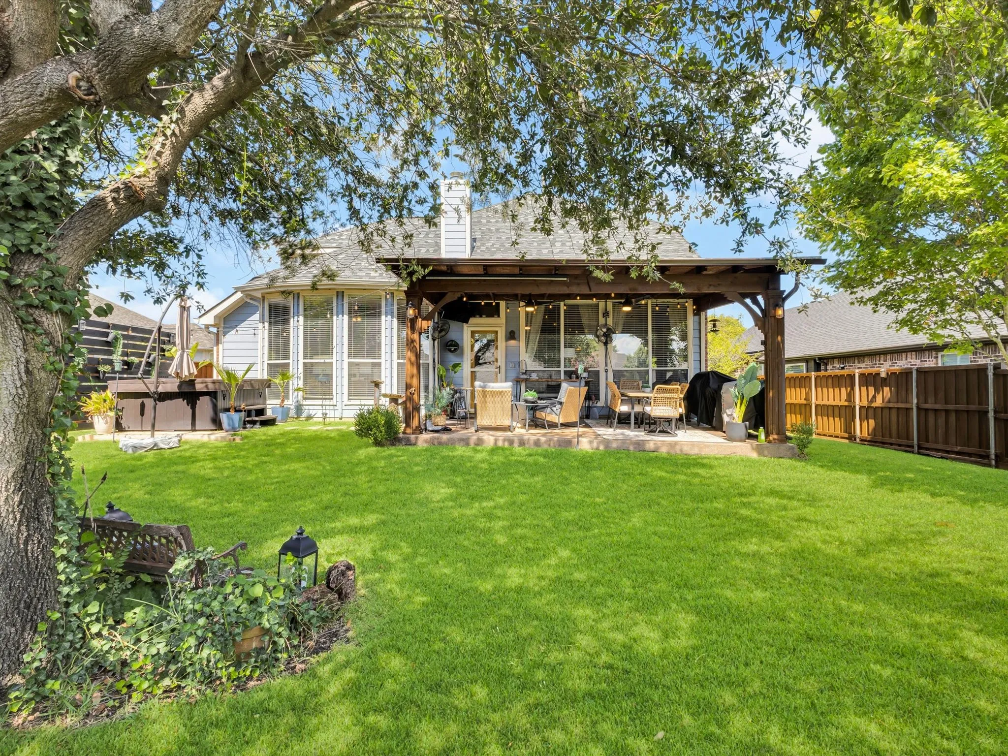 Expansive backyard featuring a manicured lawn, mature trees, and a wooden pergola covering a patio area