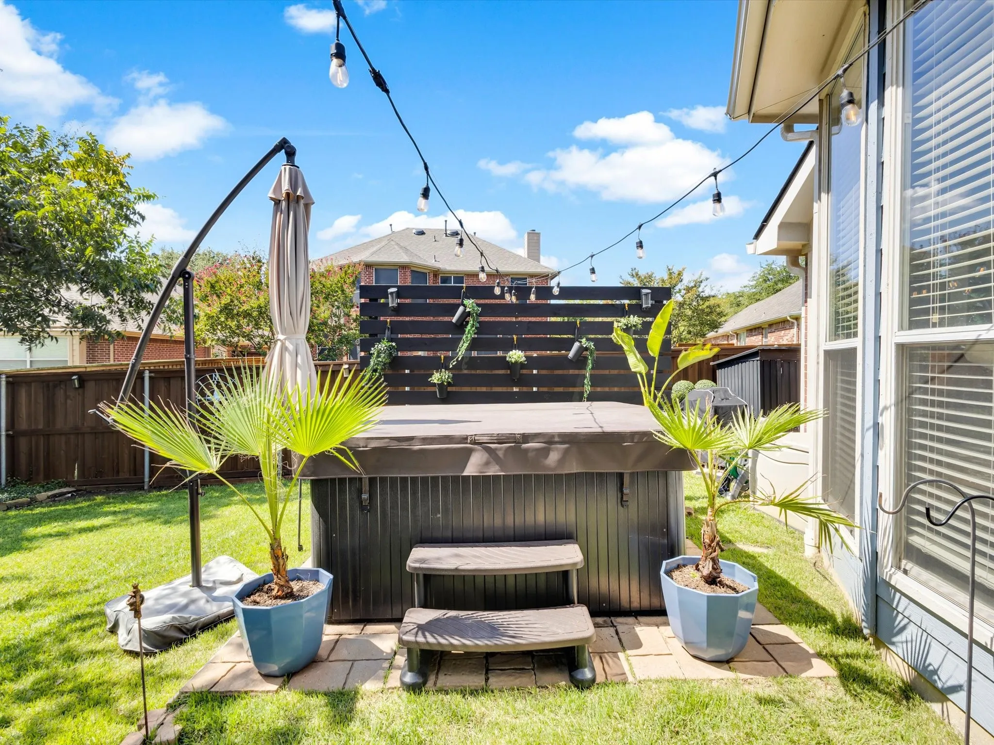 Expansive backyard featuring a hot tub with cover, string lighting, and a privacy fence