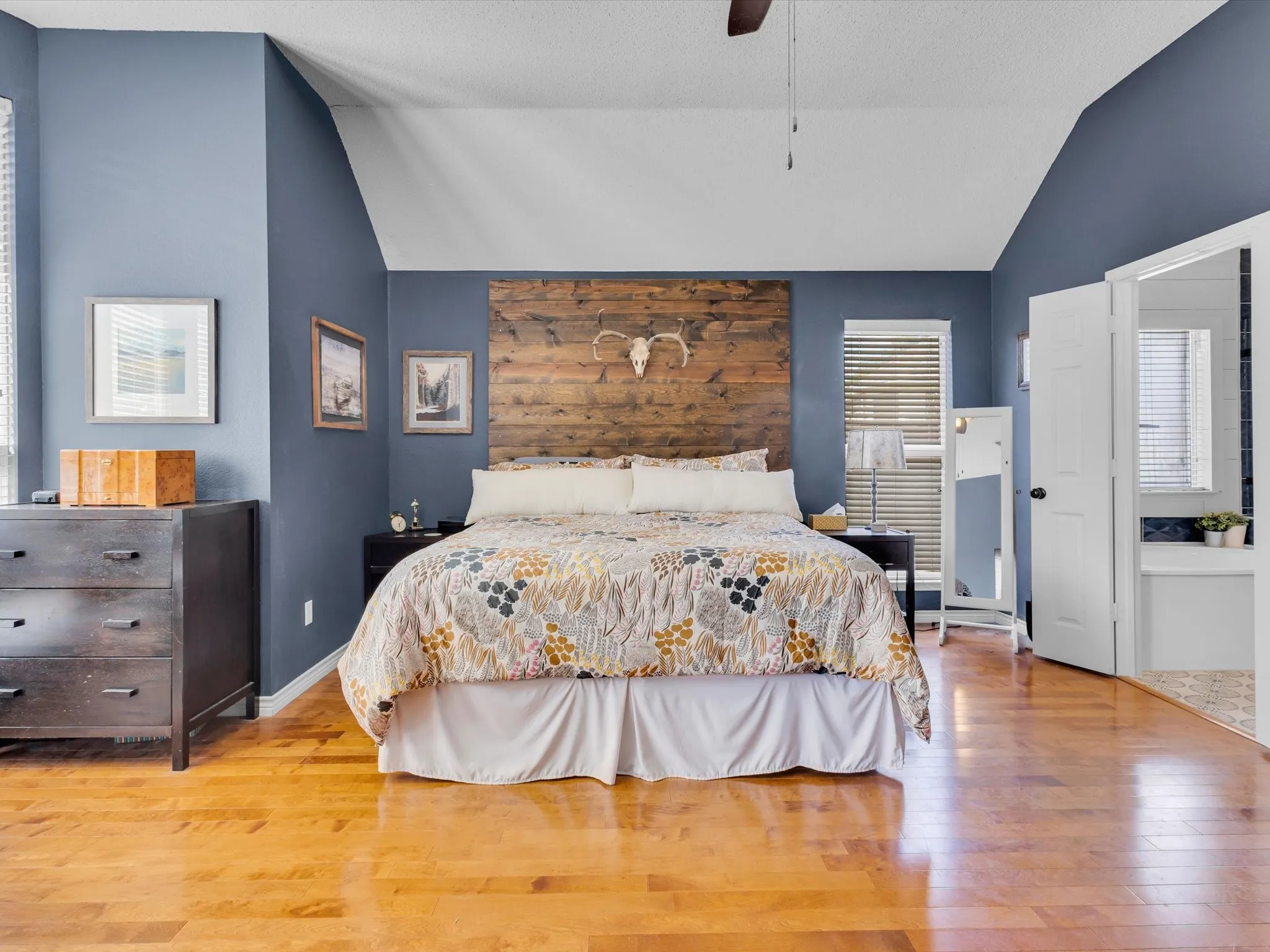 Spacious bedroom featuring vaulted ceilings, wood-finish flooring, and a unique wood plank accent wall