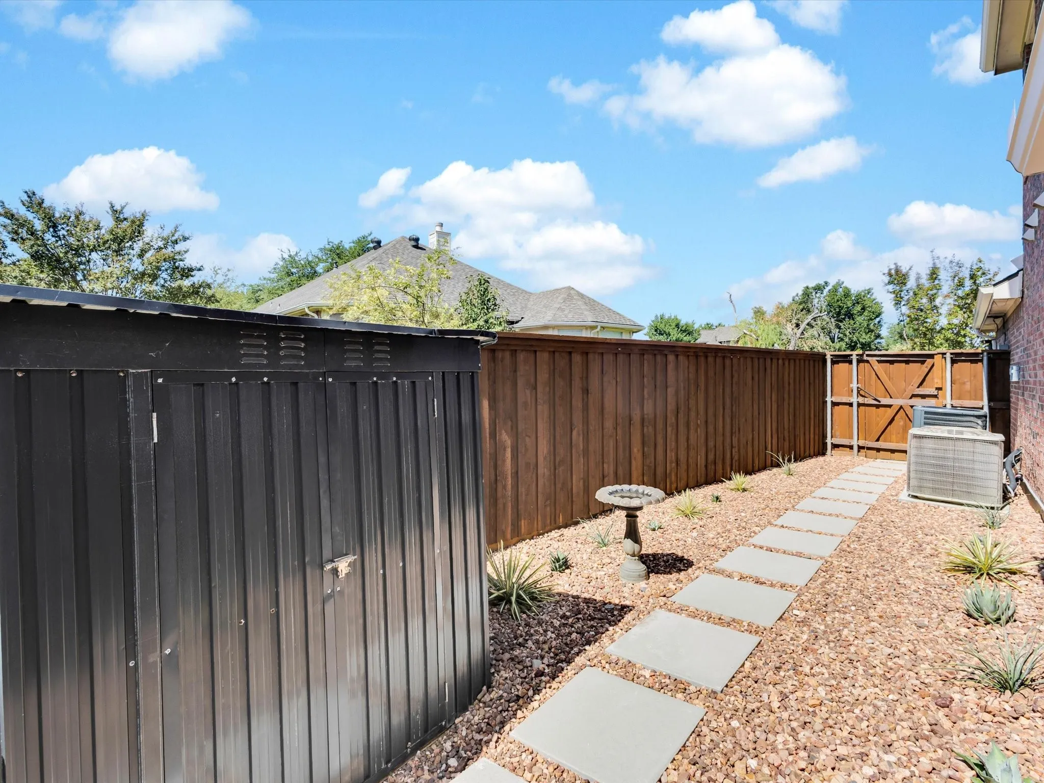 Side yard featuring a dark metal storage shed, stepping stone pathway, and gravel landscaping