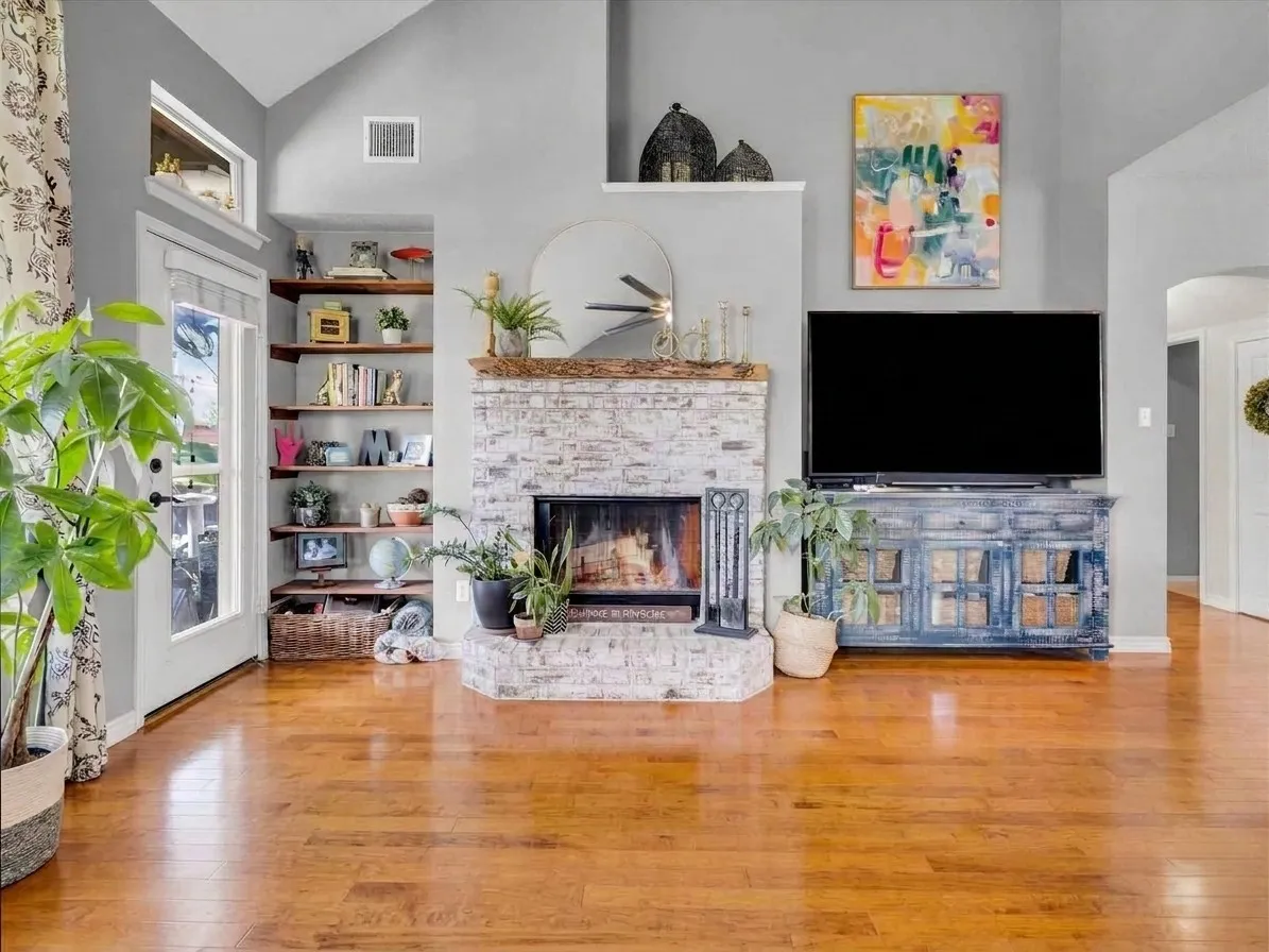 Vaulted ceiling, wood-finish flooring, white-washed brick fireplace, built-in shelving, and transom windows
