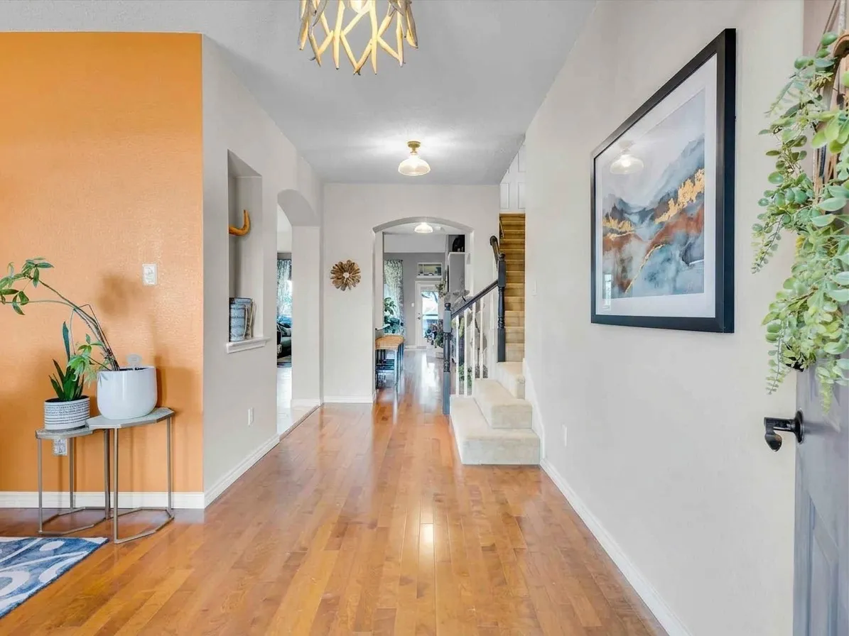 Hardwood-finish flooring extending through the hallway, showcasing arched architectural features and a staircase with carpeted treads