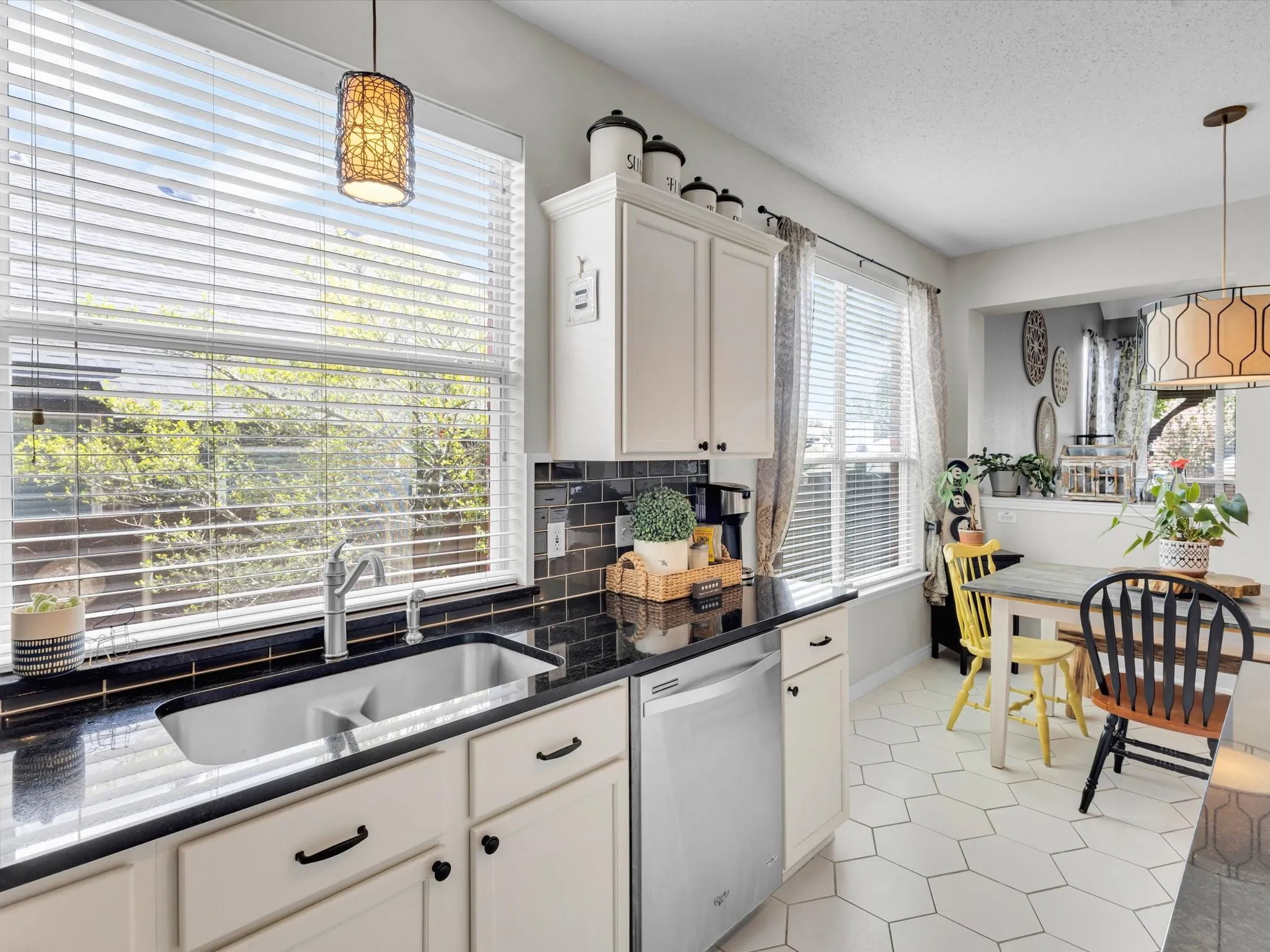 Kitchen featuring white cabinetry, black countertops, a subway tile backsplash, and a large window above the sink