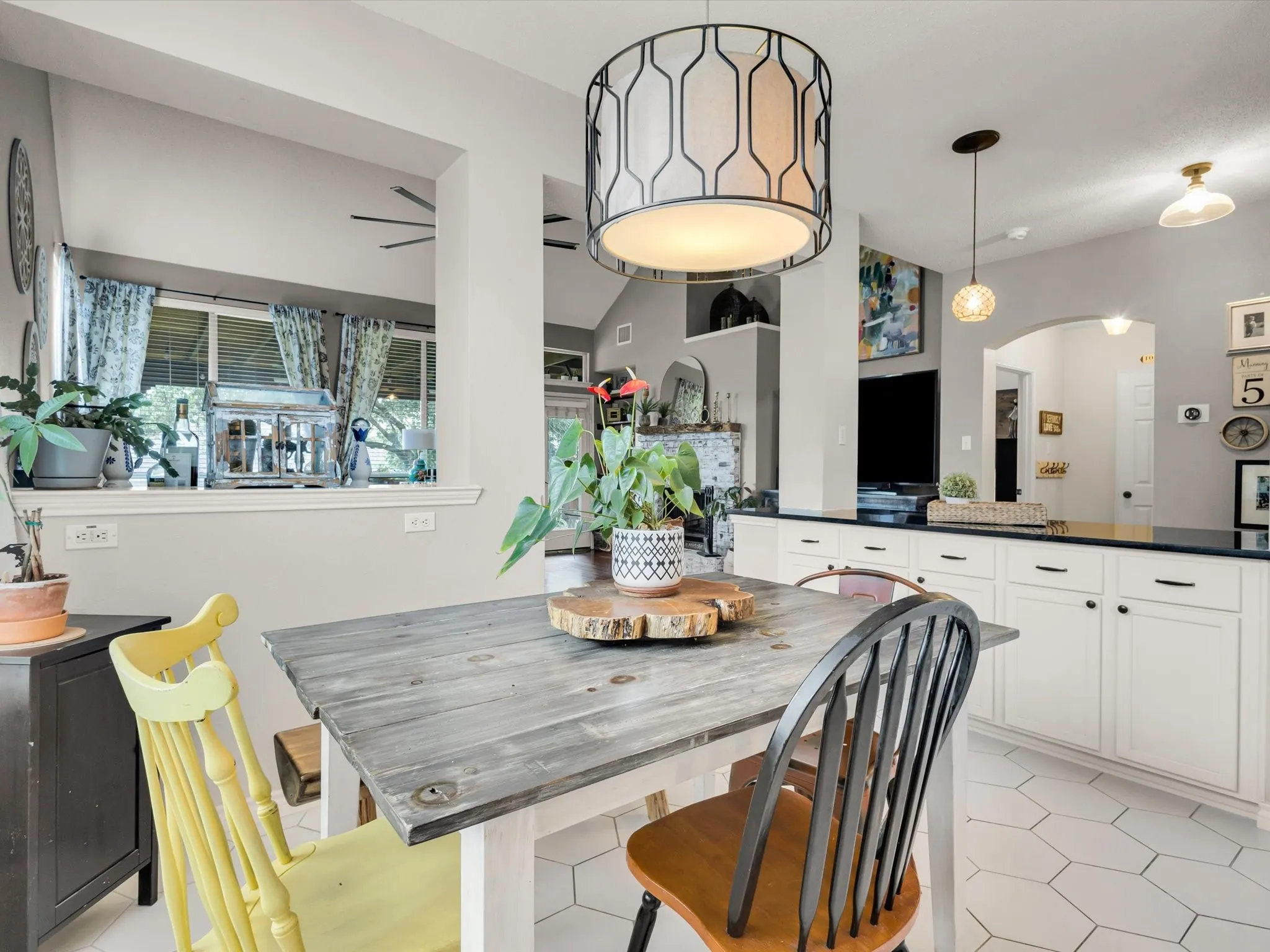 Kitchen dining area featuring a geometric pendant light fixture, white hexagonal floor tiling, and a pass-through window opening