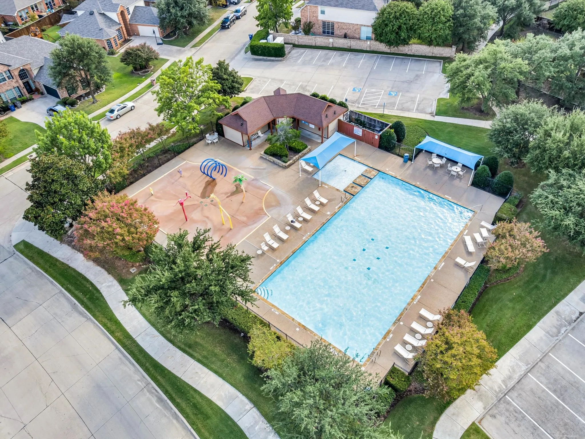 Community swimming pool with an adjacent splash pad, surrounding lounge chairs, and shaded outdoor seating